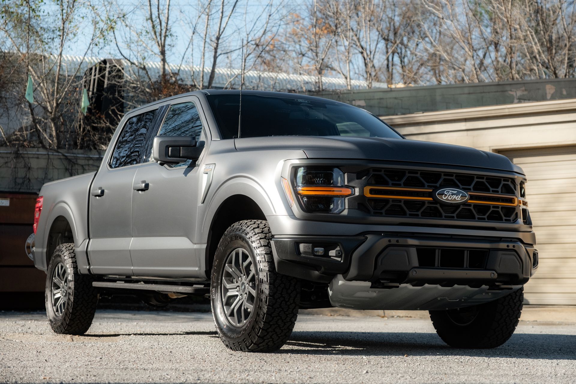 Gray lifted pickup truck parked outdoors on a gravel lot with trees in the background