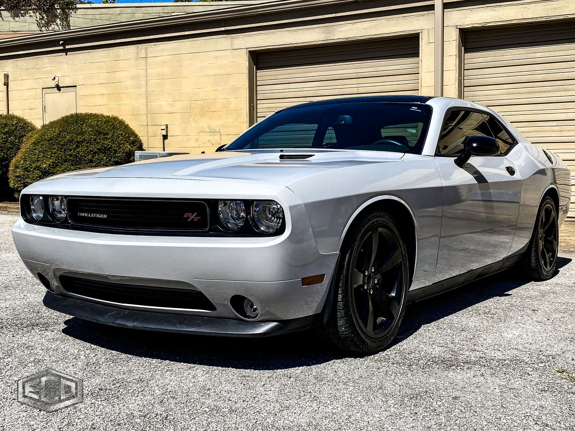 Silver Dodge Challenger parked on gravel in front of a beige building, front-left view