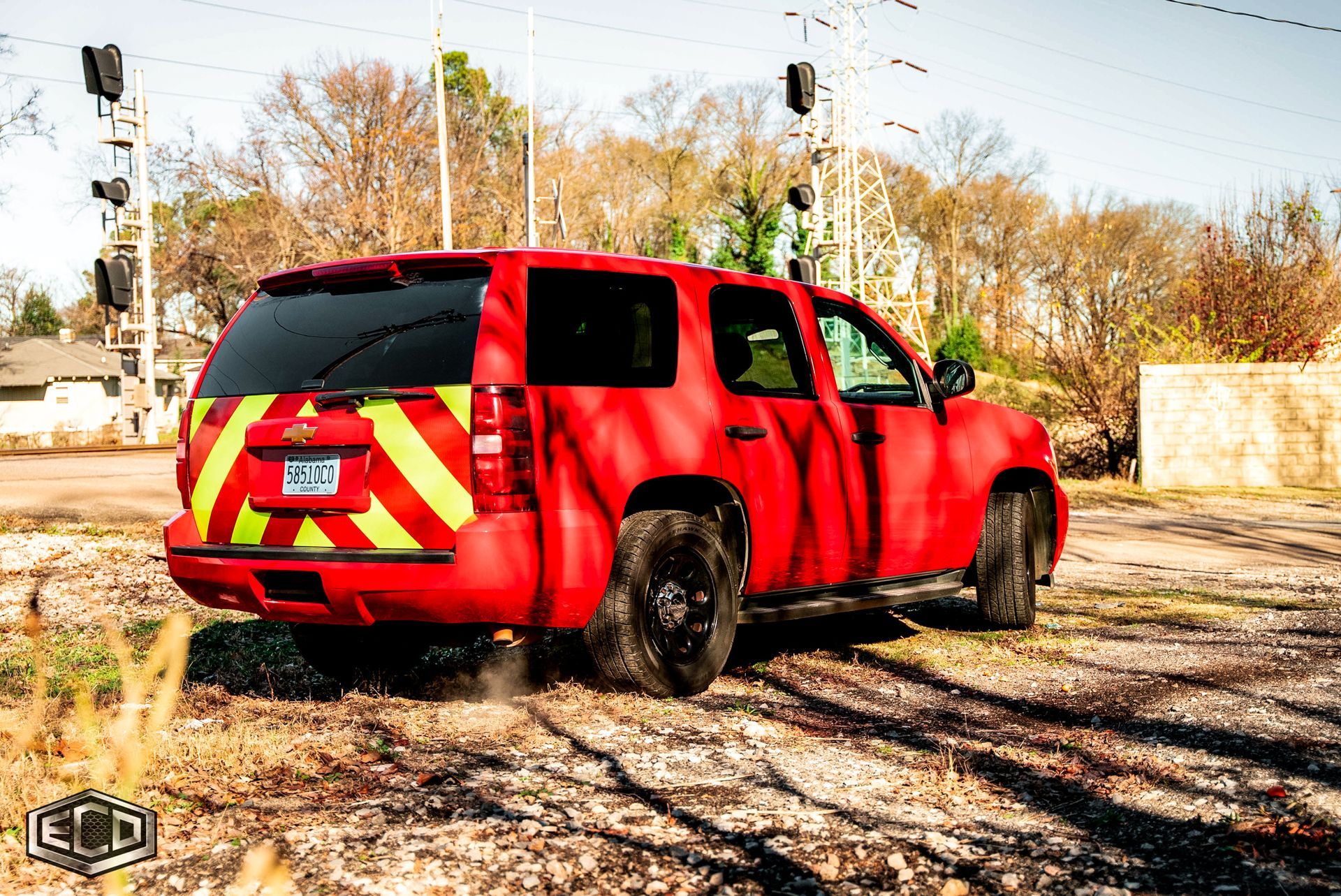 Red emergency SUV with hazard stripes parked on a dirt lot in autumn.
