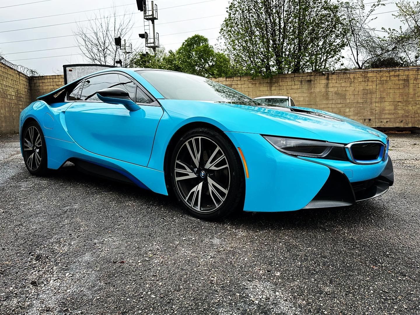 Bright blue sports car parked on gravel outdoors under an overcast sky