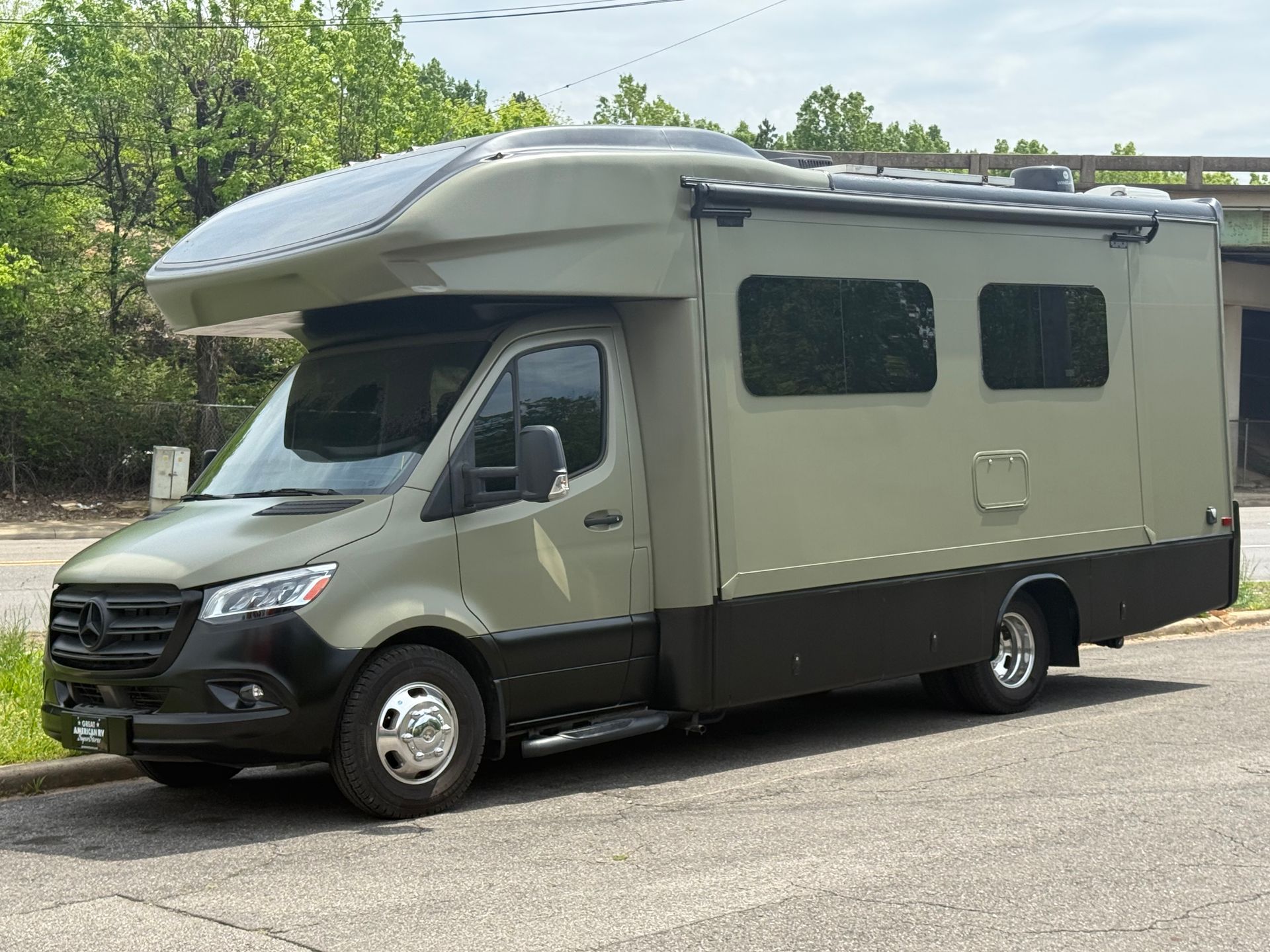 Gray and black camper van parked on a road beside trees, with rooftop storage and side windows.