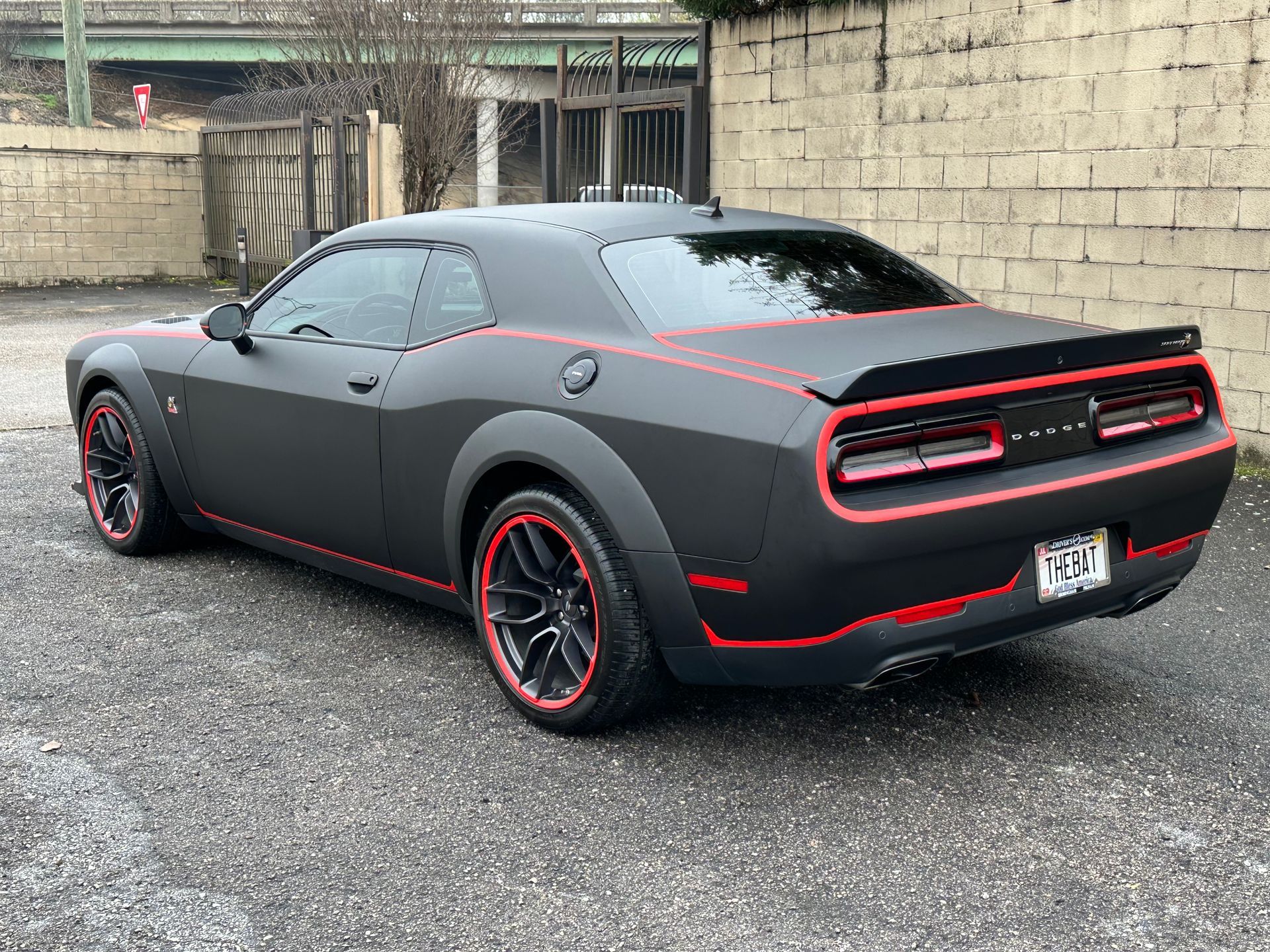 Black Dodge Challenger with red accents parked on gravel beside a brick wall.