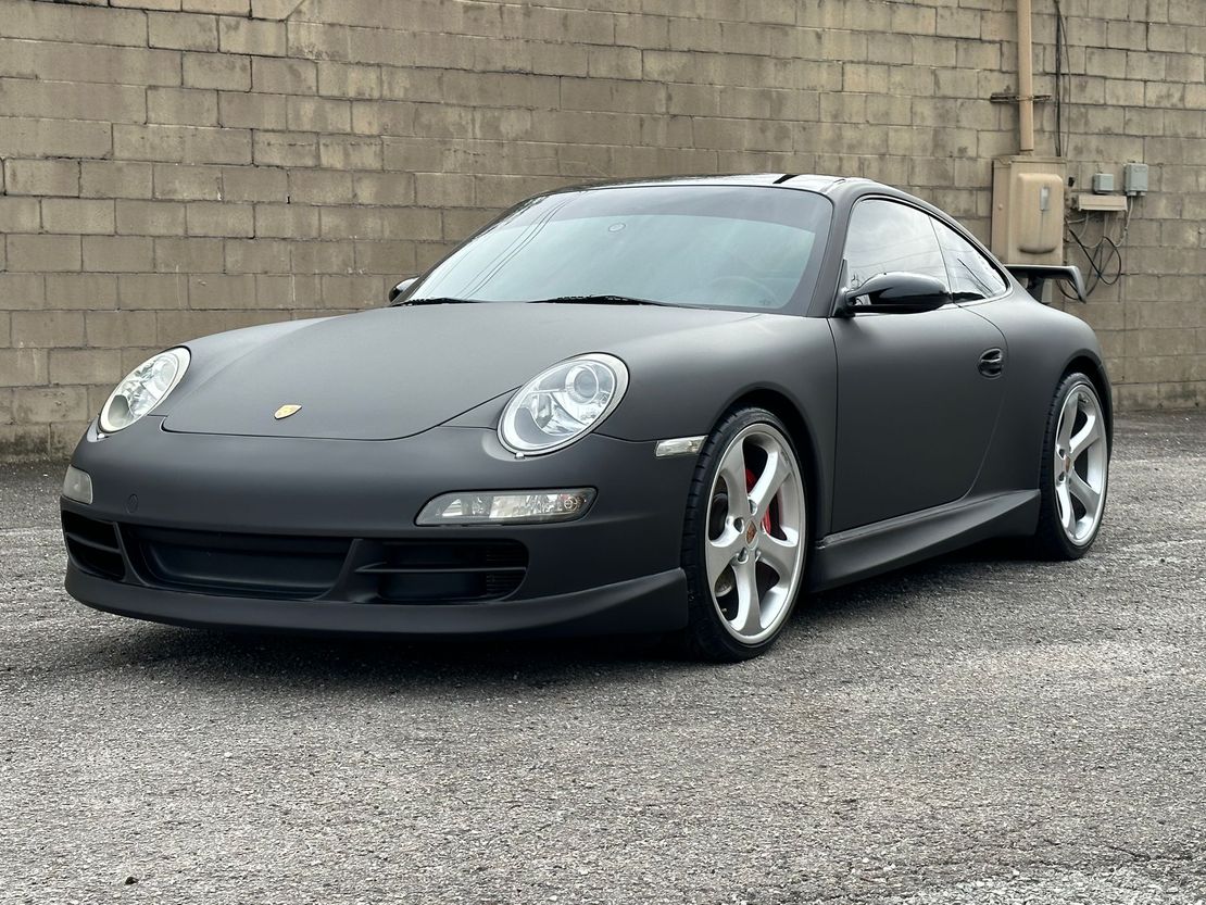Dark gray Porsche sports car parked on gravel in front of a cinderblock wall