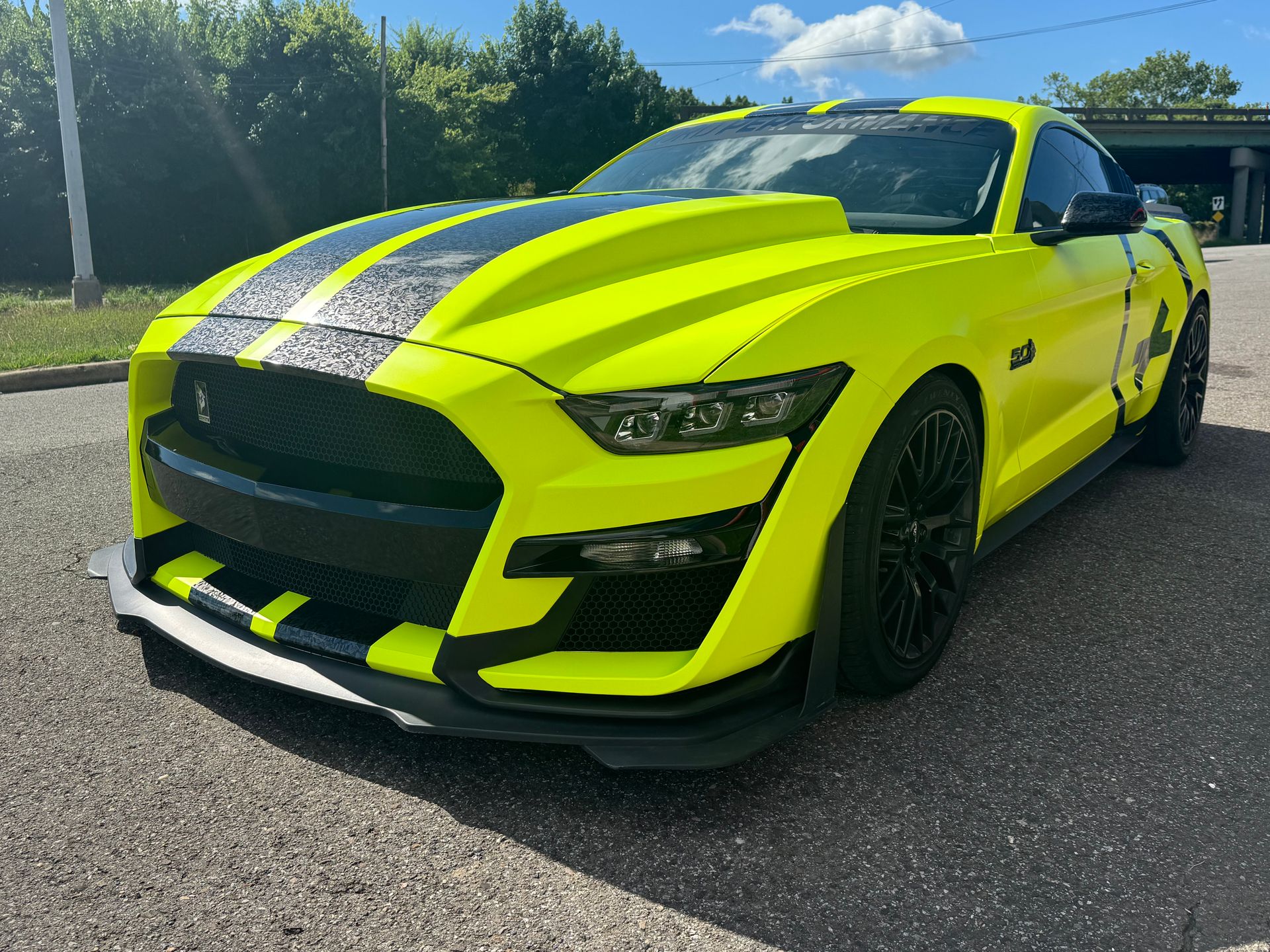 Neon yellow sports car with black racing stripes parked on a road outdoors.
