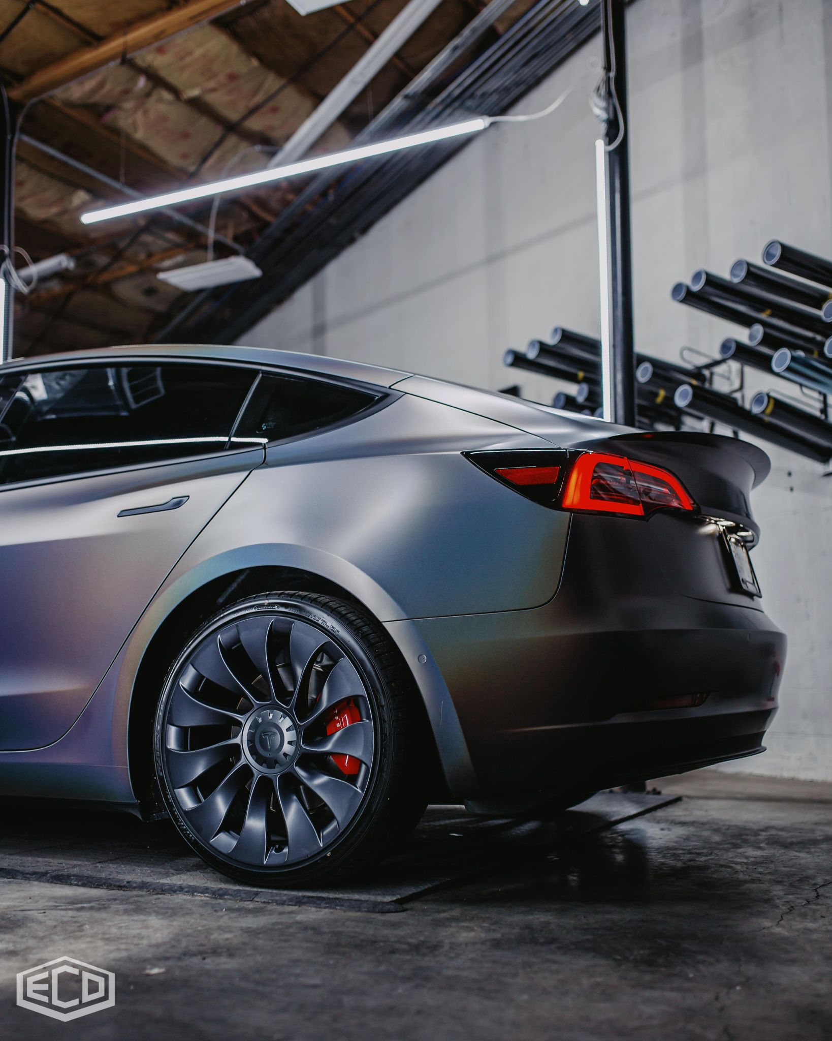 Black sedan with dark rims parked in an industrial garage, rear side view.