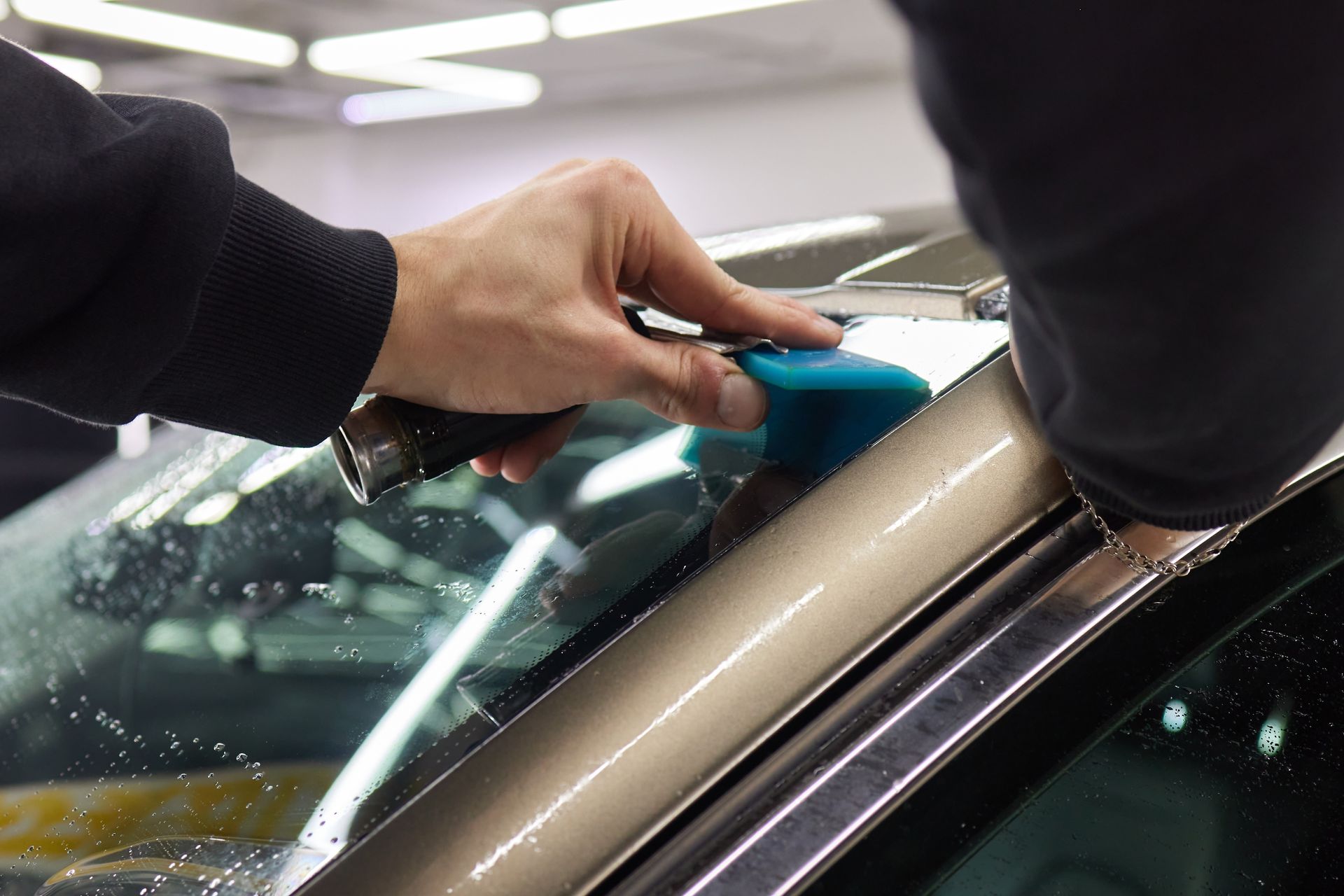 Hands using a blue squeegee to apply window film on a car windshield
