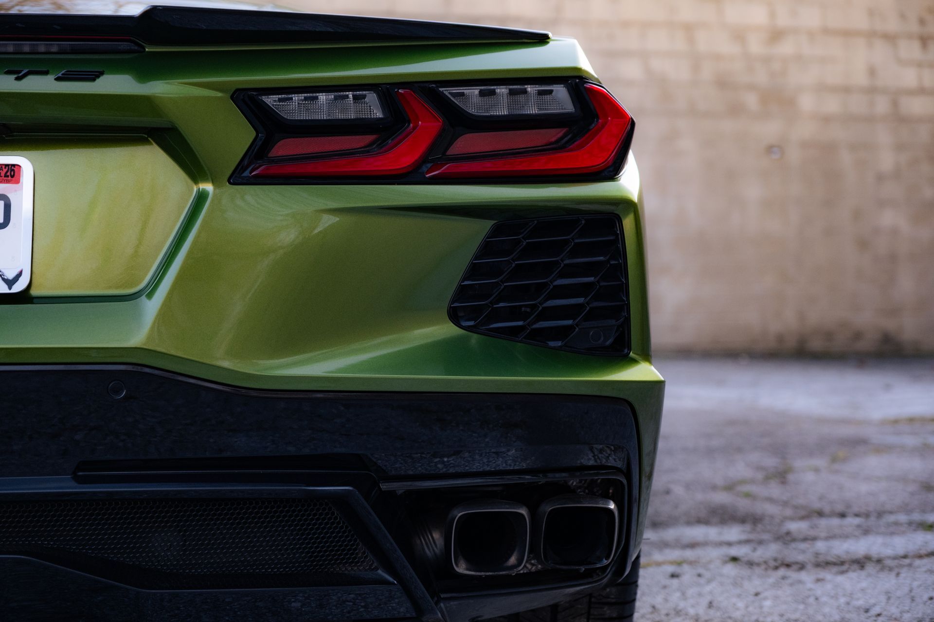 Rear view of a green sports car with red taillights, parked on pavement near a wall.