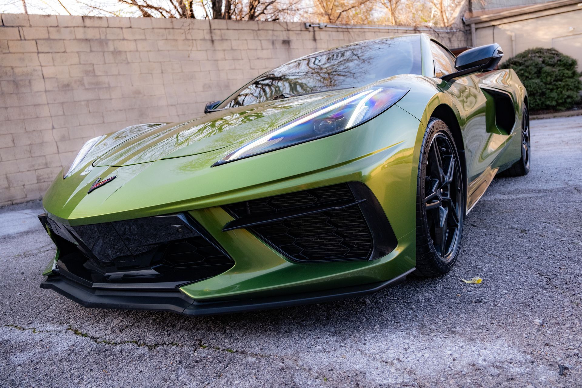 Green Lamborghini sports car parked on gravel beside a stone wall, front-left view
