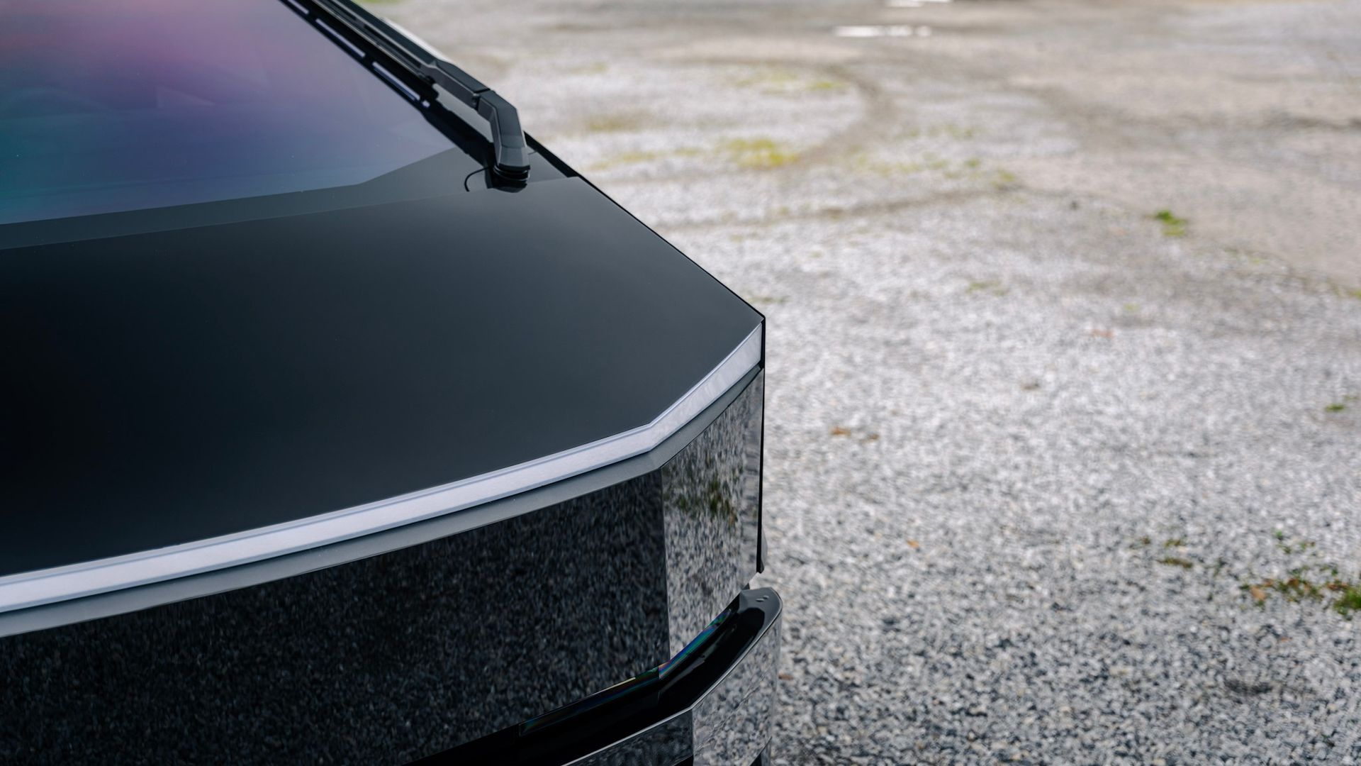 Close-up of a black car’s front corner with windshield wiper on a gravel surface