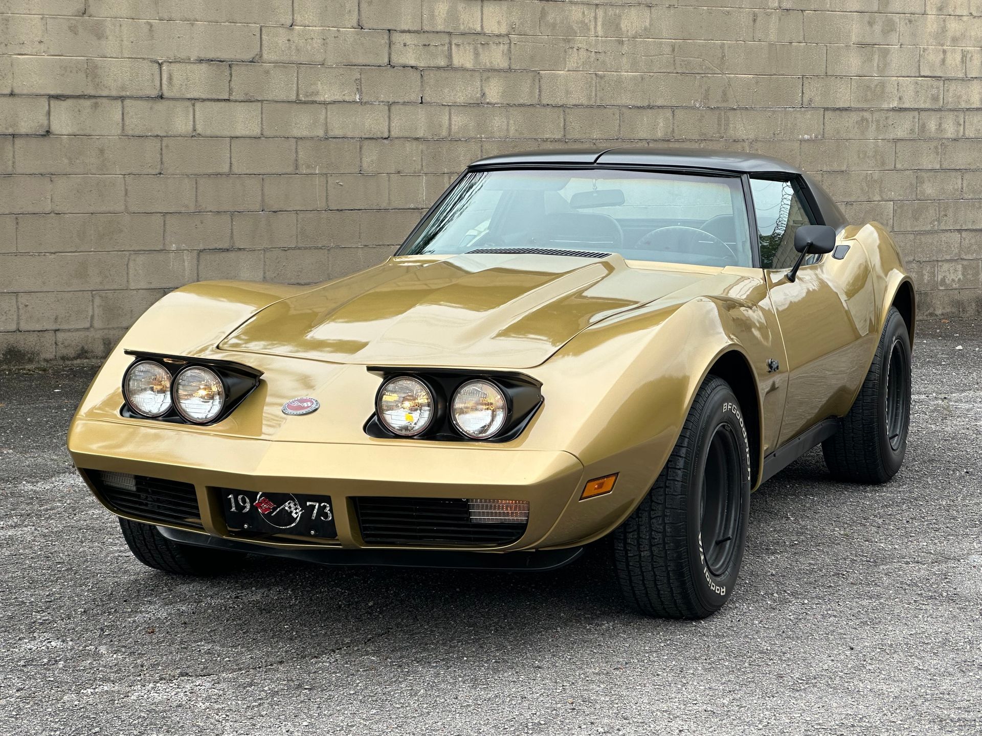 Gold classic sports car parked on gravel in front of a concrete wall