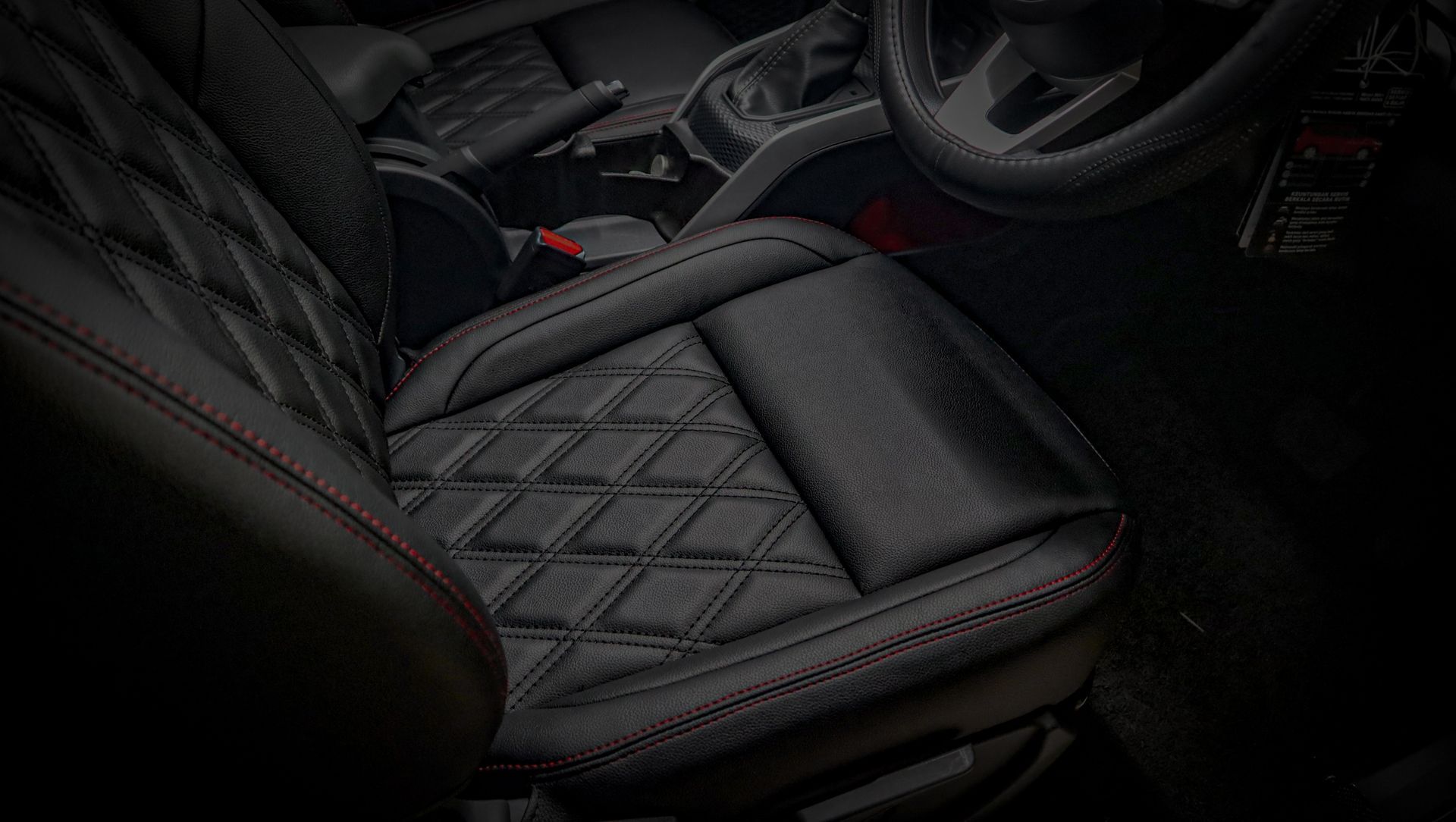 Black car interior with a quilted leather seat and red stitching, seen from the front cabin
