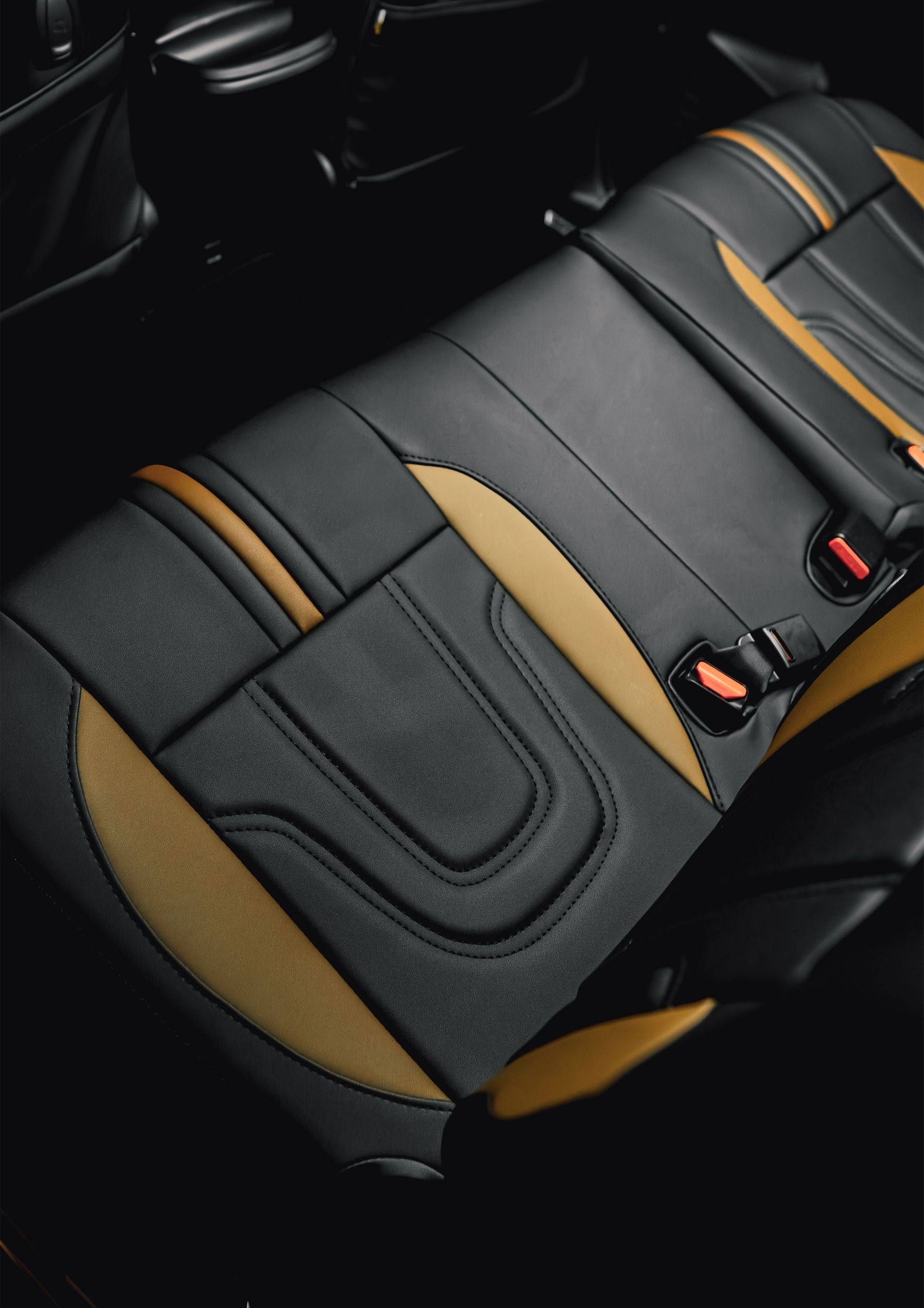 Black car seat cover with tan accents and orange stitching, shown on a rear seat.