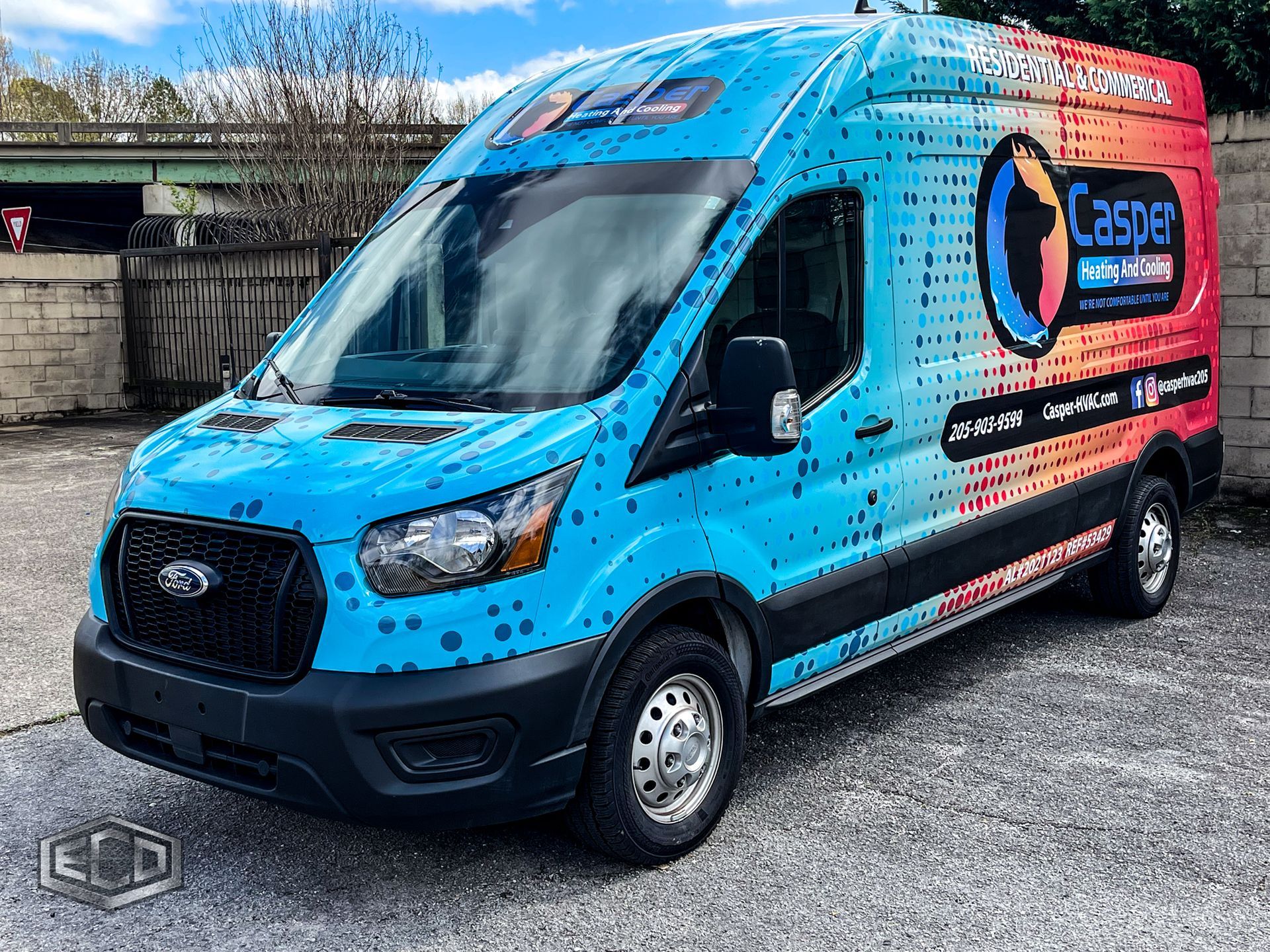 Blue Ford van with colorful advertising wrap parked outdoors on a street.