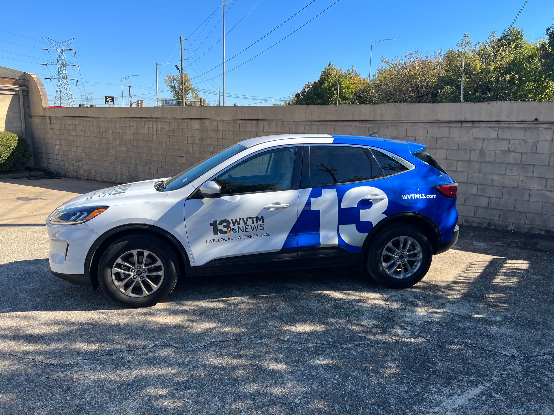 Blue-and-white SUV with large number 13 parked beside a concrete wall on a sunny lot
