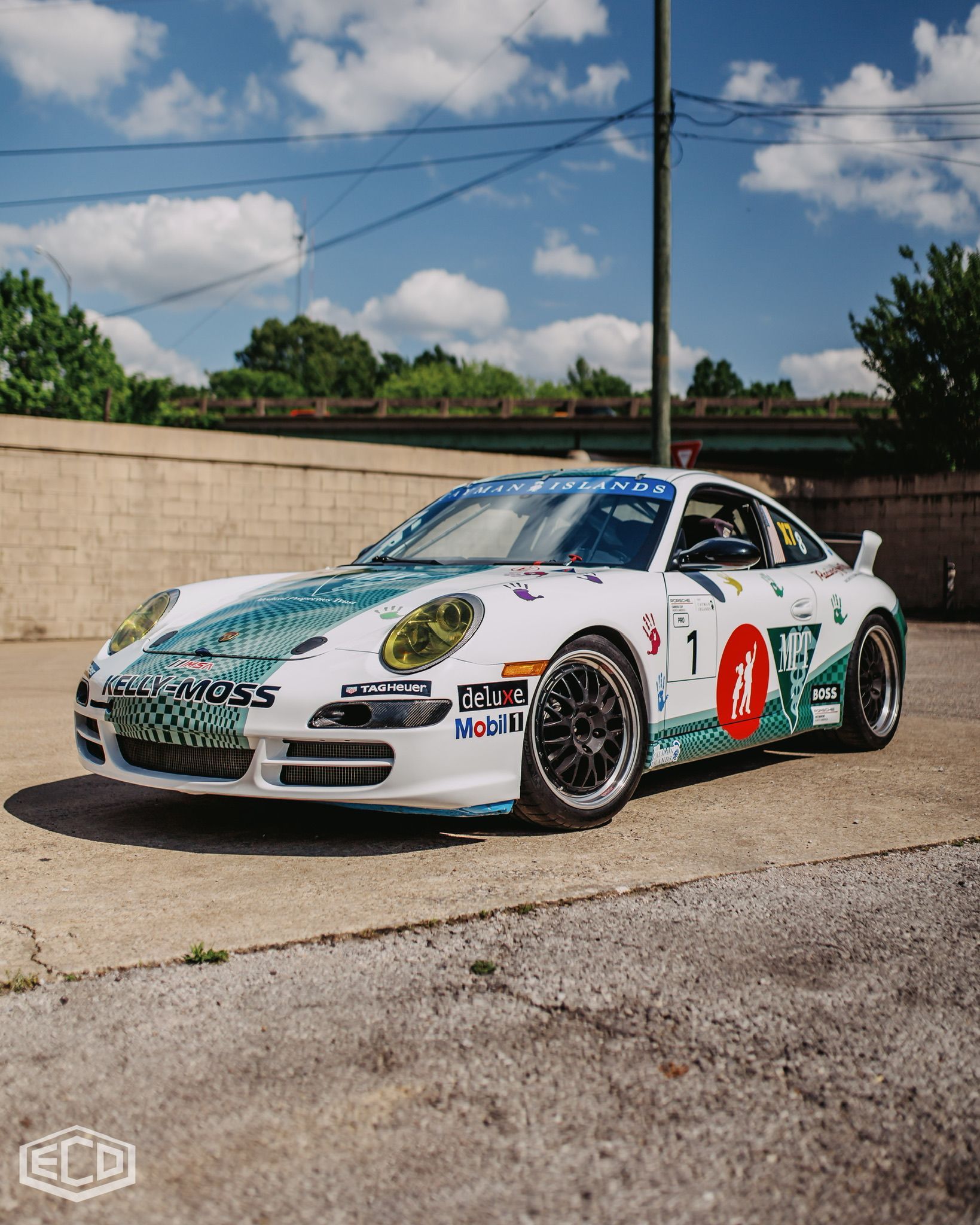 White and green race car with number 1 parked outdoors beside a brick wall under a blue sky