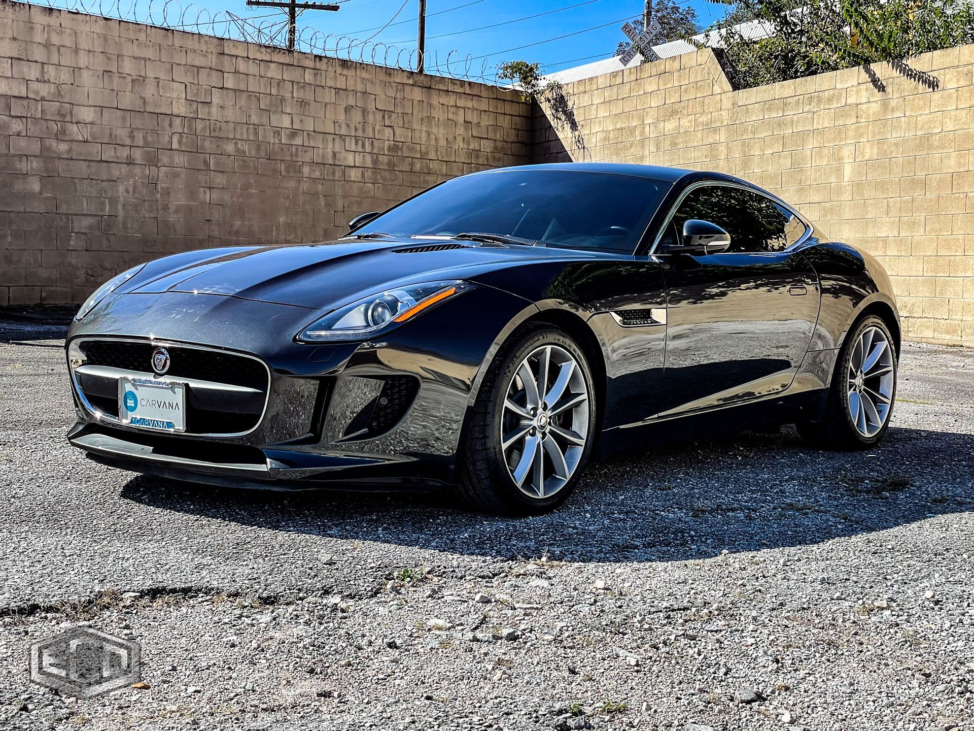 Black Nissan sports coupe parked on gravel in front of a tan wall under a blue sky