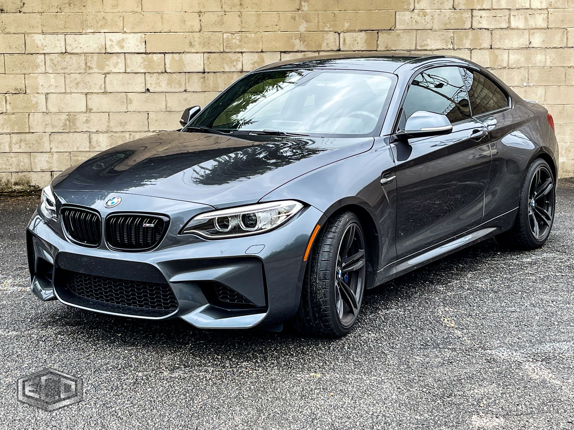 Gray BMW coupe parked on gravel in front of a beige brick wall