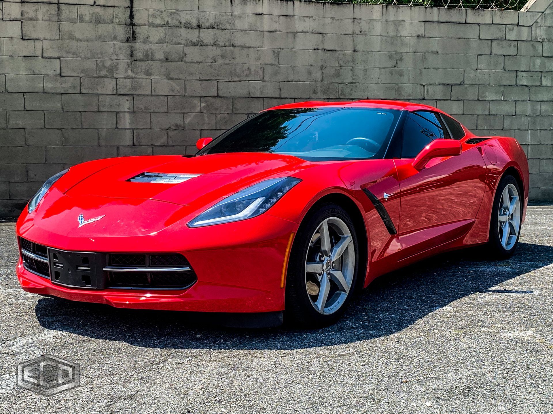 Red sports car parked on gravel in front of a cinder block wall.
