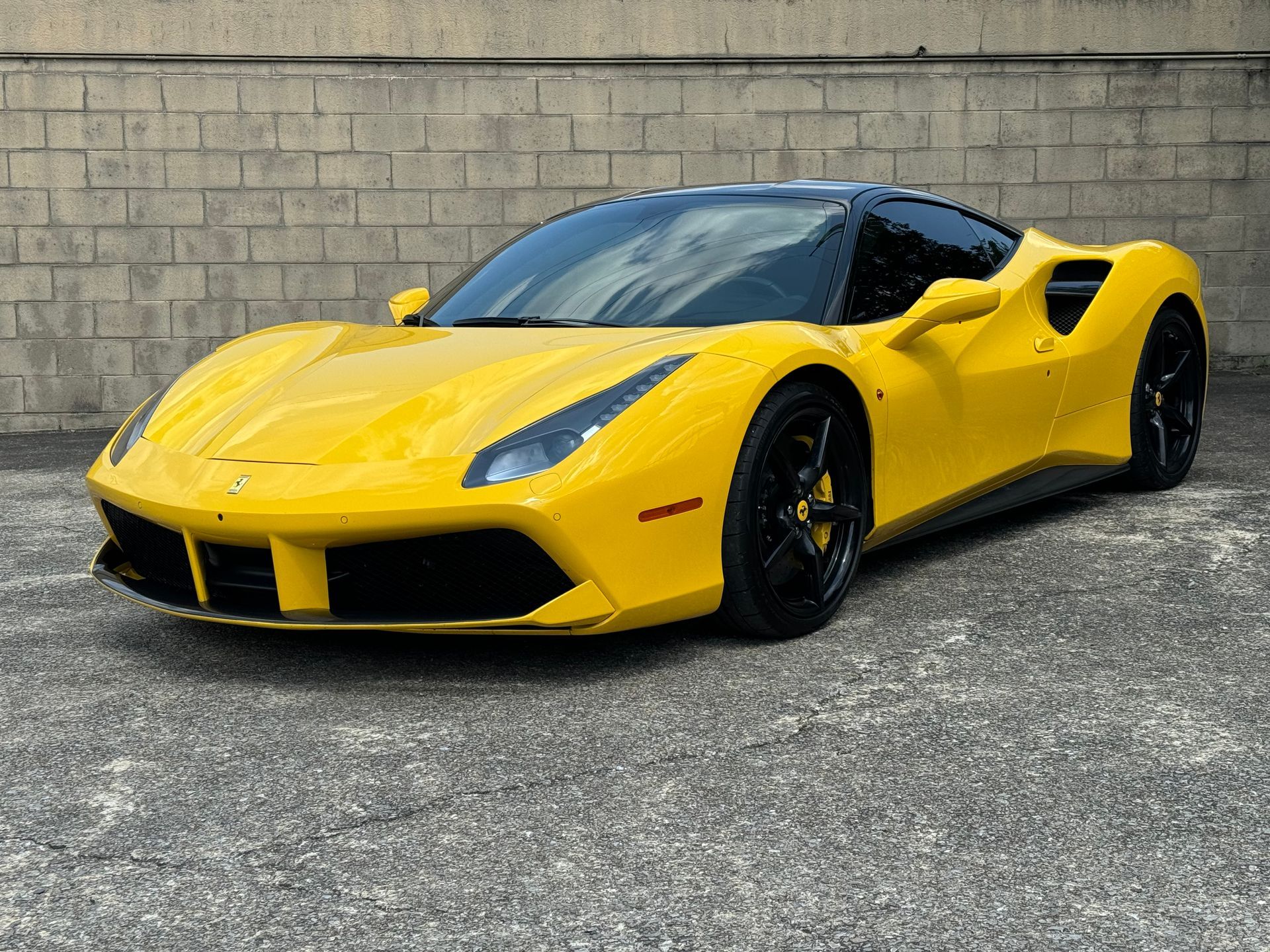 Yellow sports car parked on asphalt in front of a concrete wall