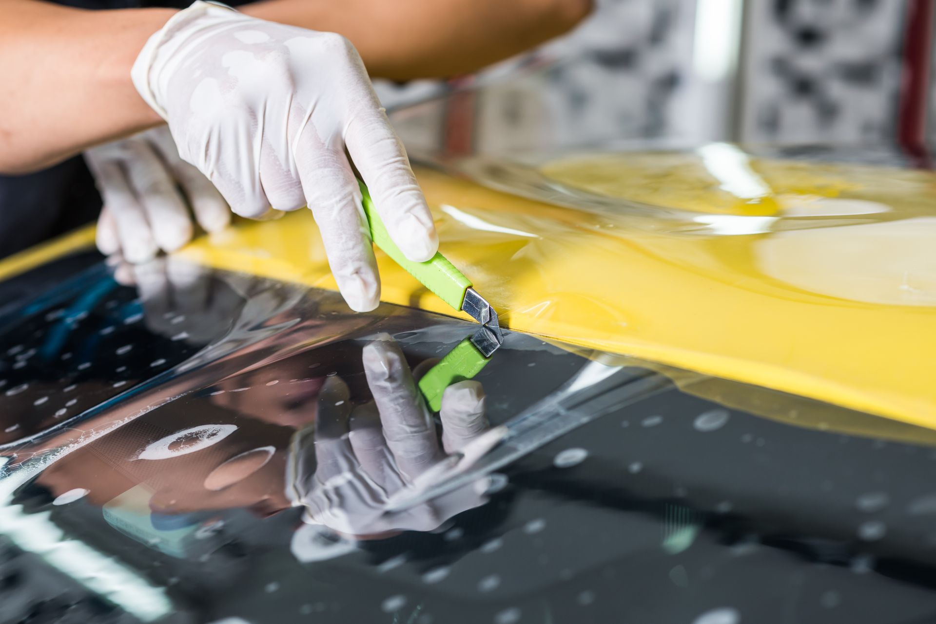 Gloved hand scraping yellow film from a car windshield with a razor blade