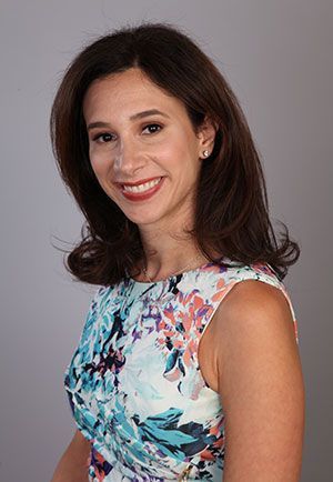 Smiling woman in a floral dress posing against a gray background