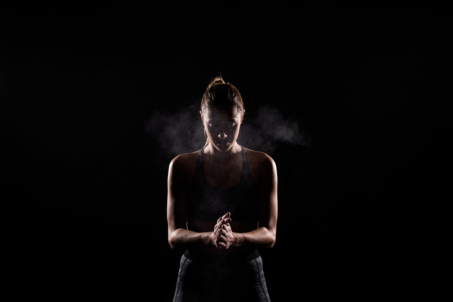A person in athletic wear clapping hands, releasing chalk into the air against a dark backdrop. A person in athletic wear clapping hands, releasing chalk into the air against a dark backdrop.