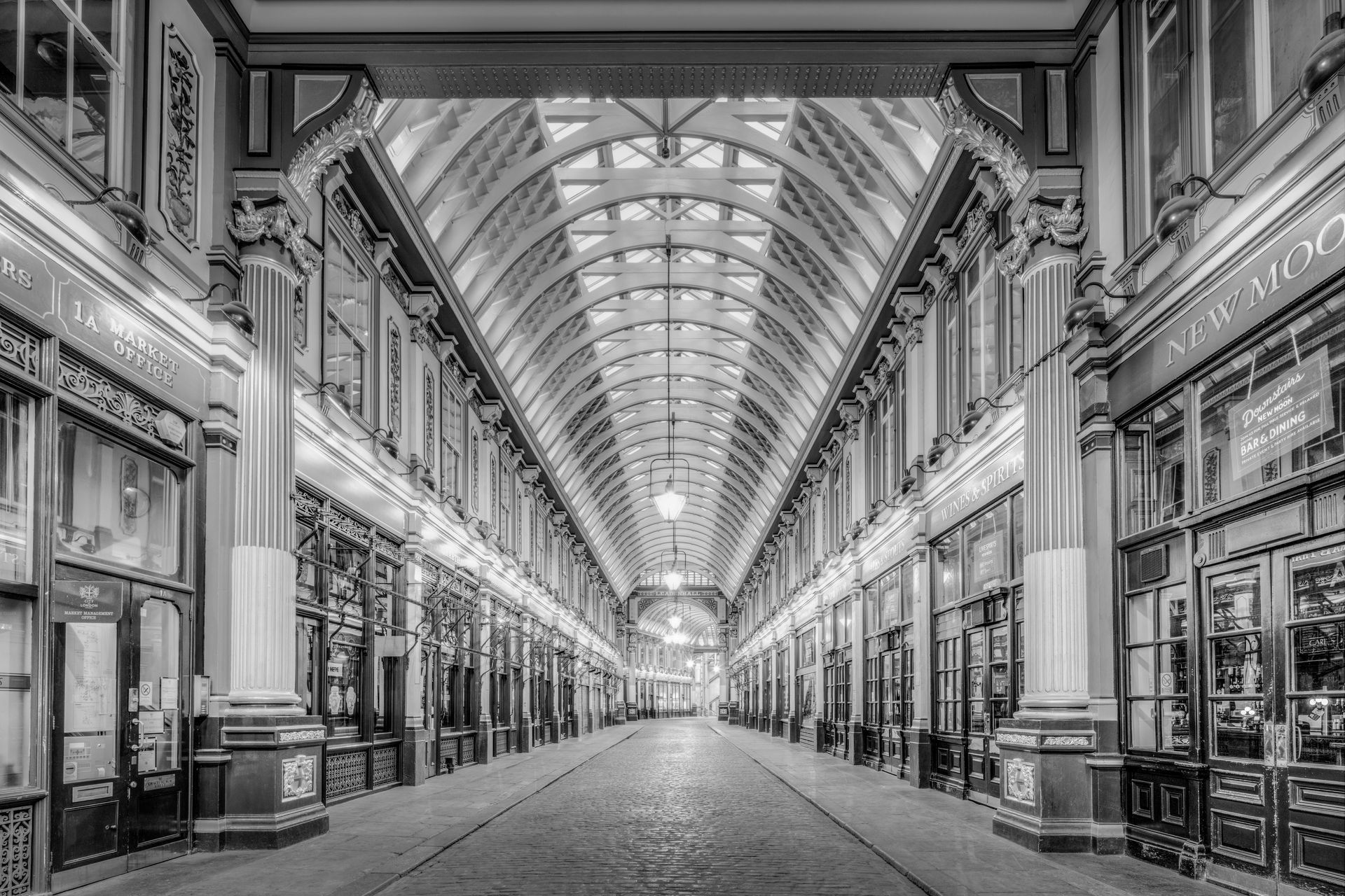 A long, symmetrical indoor shopping arcade with arched glass ceiling, black and white.