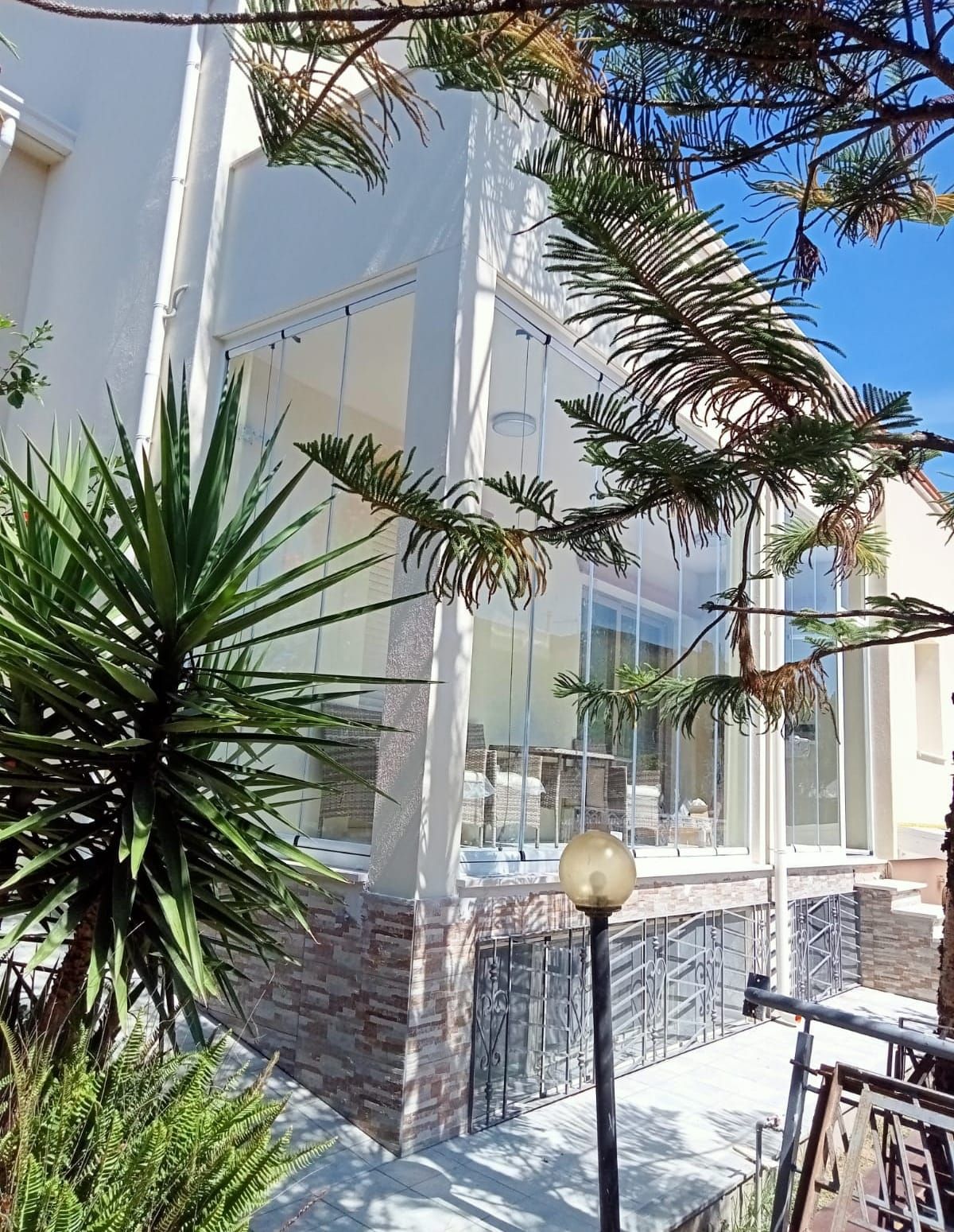 Edificio con veranda chiusa in vetro, dettagli in pietra e piante, visto da un'angolazione leggermente elevata.
