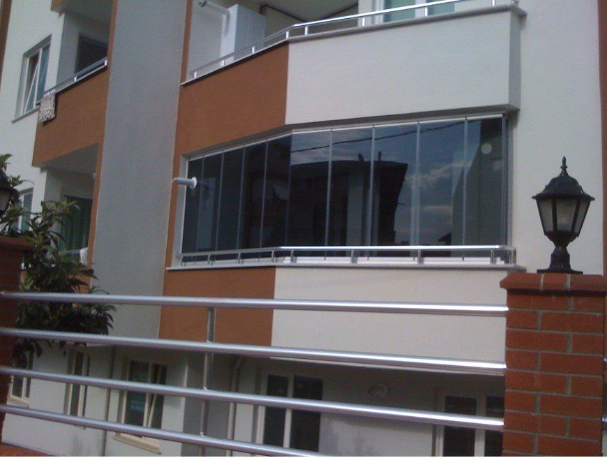 Esterno di un condominio con balcone in vetro, ringhiera in acciaio inossidabile e pilastro in mattoni con lampada.