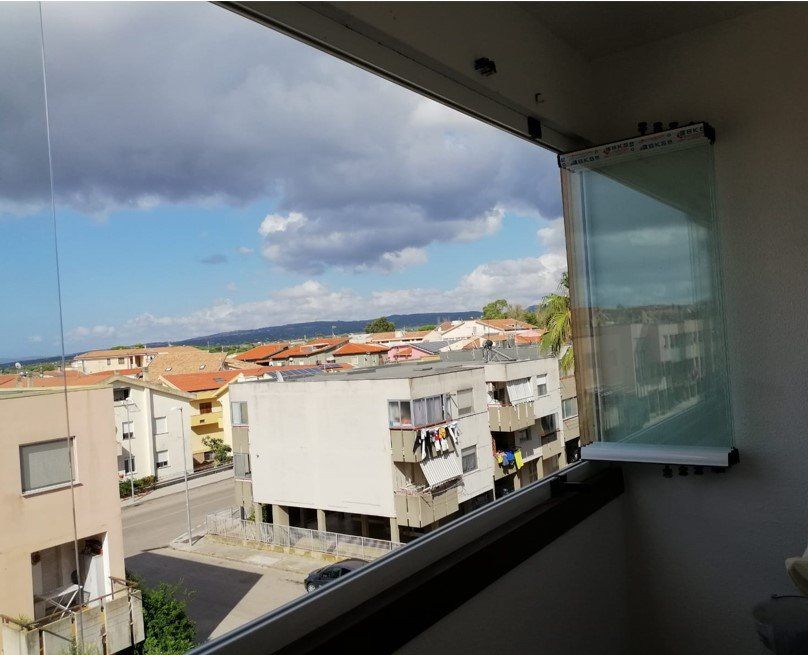 Le porte-finestre in vetro del balcone si aprirono, dando sulla vista degli edifici, della strada e del cielo nuvoloso.