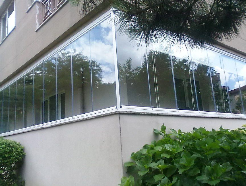 Balcone con vetrate e cornice bianca su un edificio. Cielo coperto riflesso nel vetro.