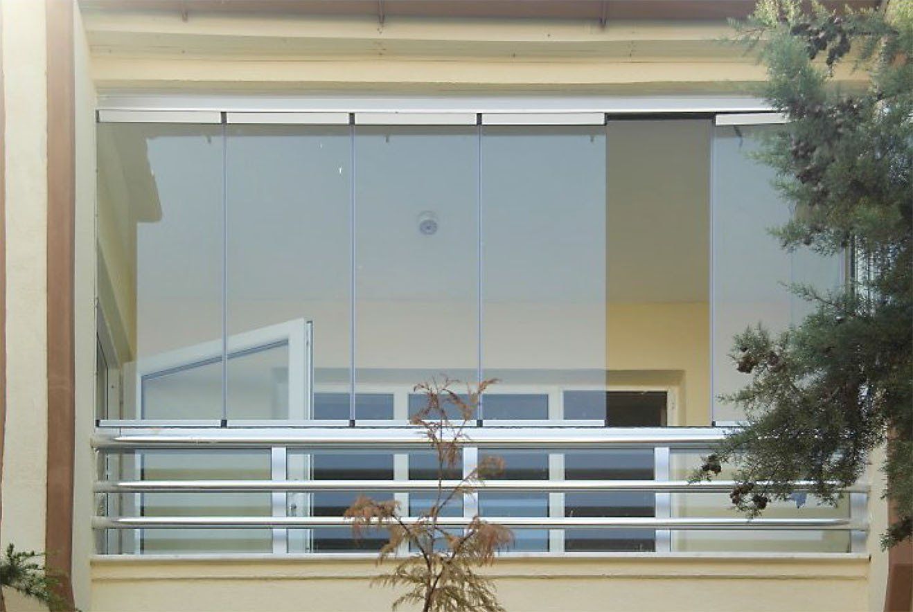 Balcone con vetrata, ringhiera orizzontale e alberi.