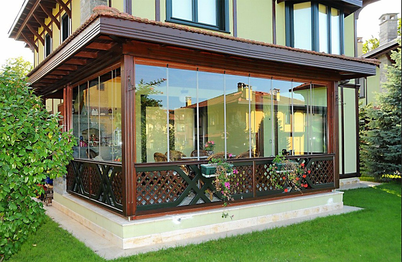Veranda con vetrate, struttura in legno e tralicci, annessa a una casa con prato verde.