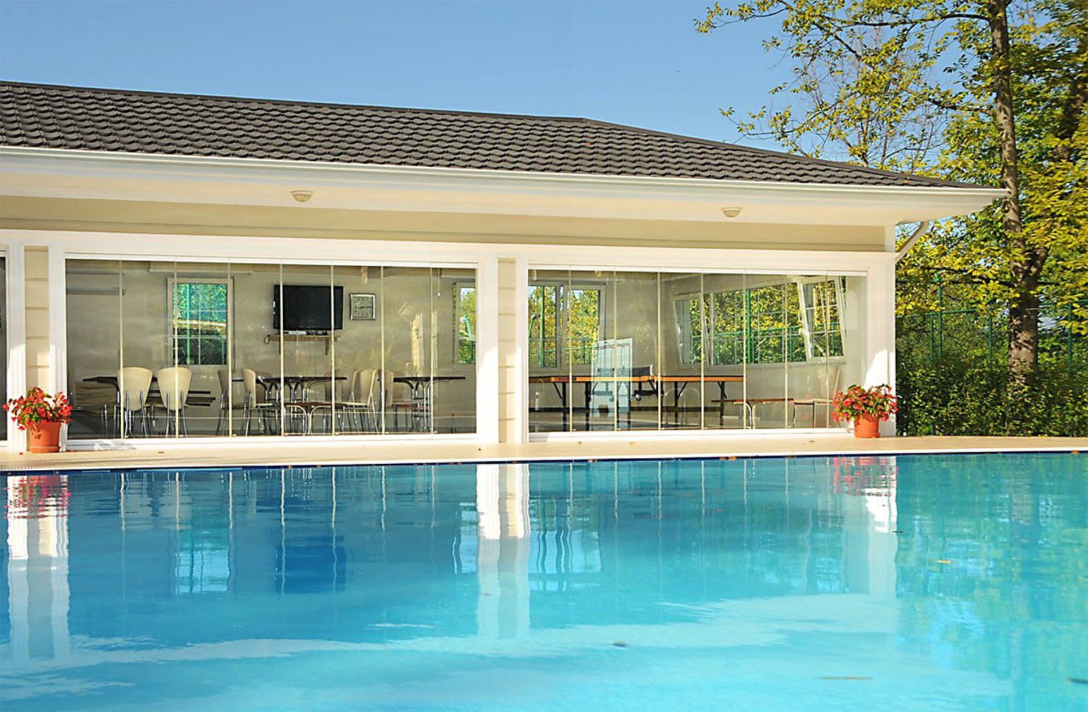 Piscina di fronte a un edificio con pareti in vetro che riflettono l'acqua blu e l'interno.
