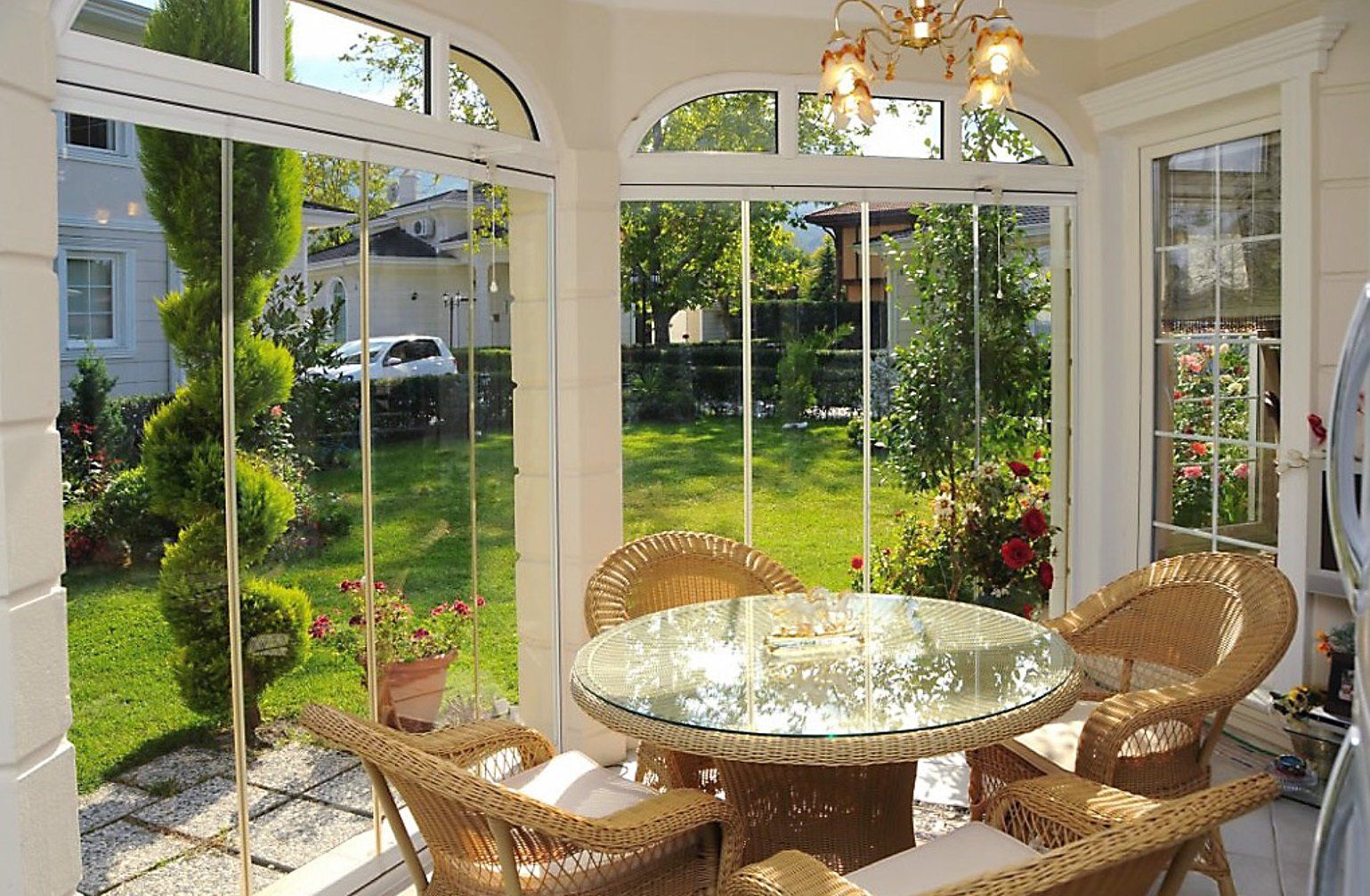 Veranda con mobili in vimini, tavolo in vetro e vista sul giardino.