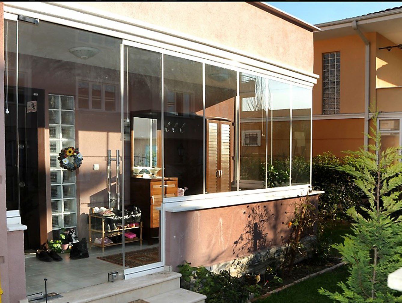 Veranda con vetrate e finiture bianche, con vista sul giardino. Pannelli e porta in vetro trasparente, interno a vista.