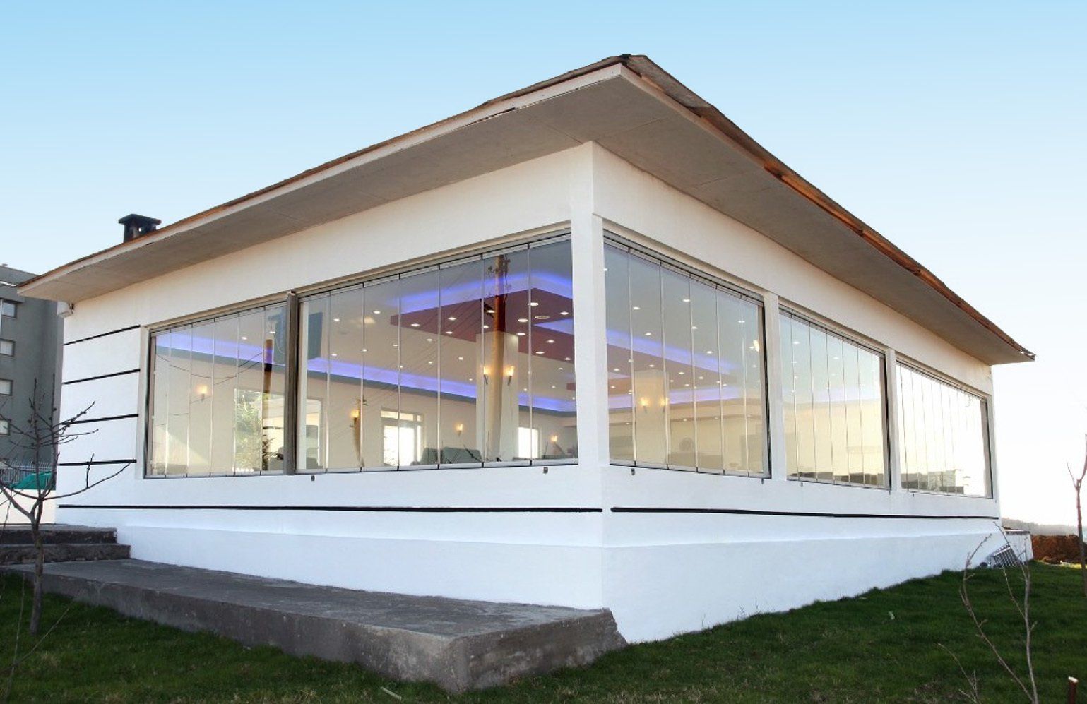 Edificio bianco con pareti in vetro, posti a sedere all'aperto, illuminazione blu e rossa, sullo sfondo di un cielo azzurro.
