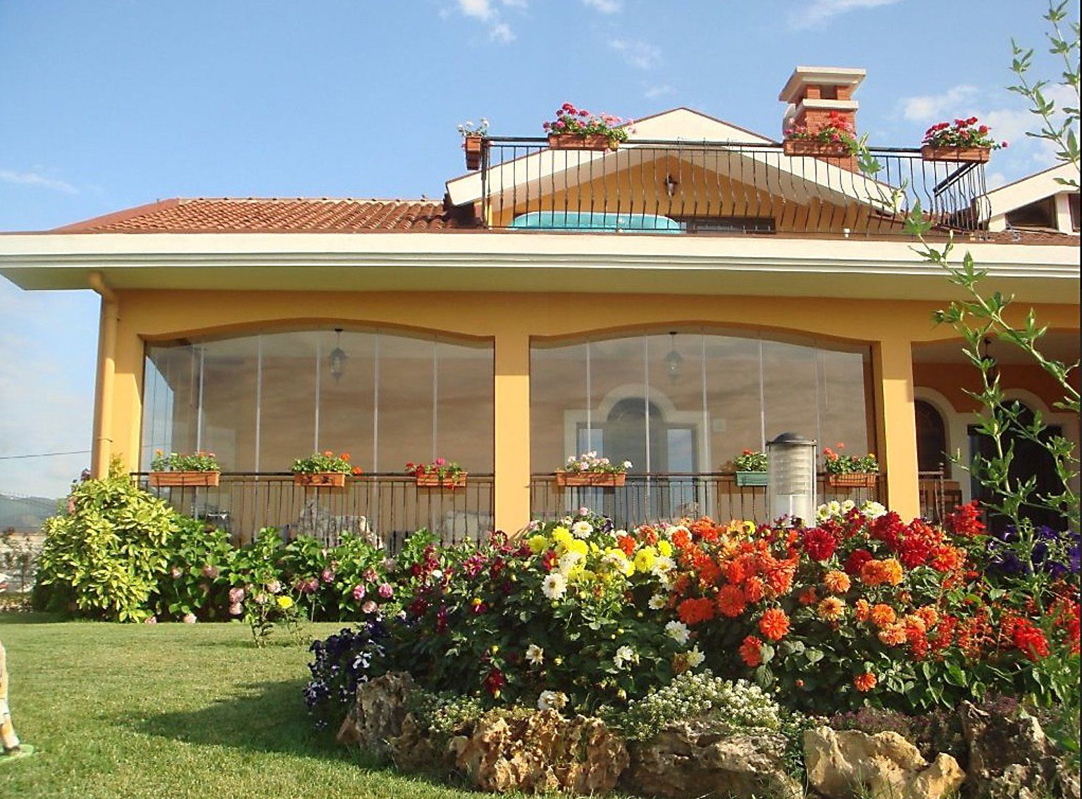 Una casa con una facciata soleggiata, una veranda coperta e un vivace giardino fiorito.
