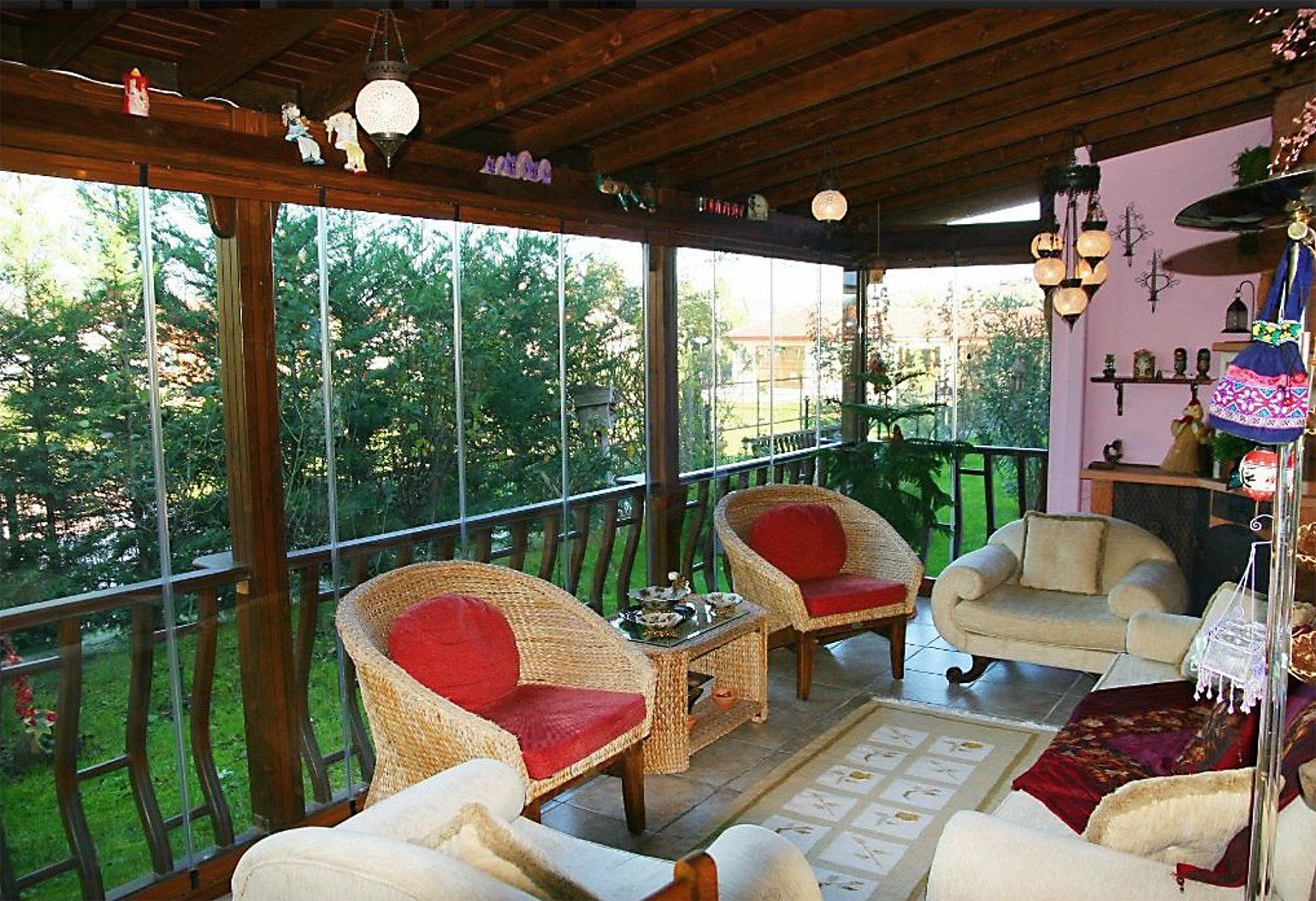 Veranda chiusa con sedie in vimini, pareti in vetro e vista su un cortile verde.