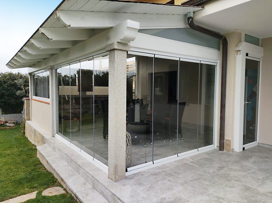 Veranda chiusa da vetrate con finiture bianche, colonne in pietra grigia e tetto bianco. Prato a vista.