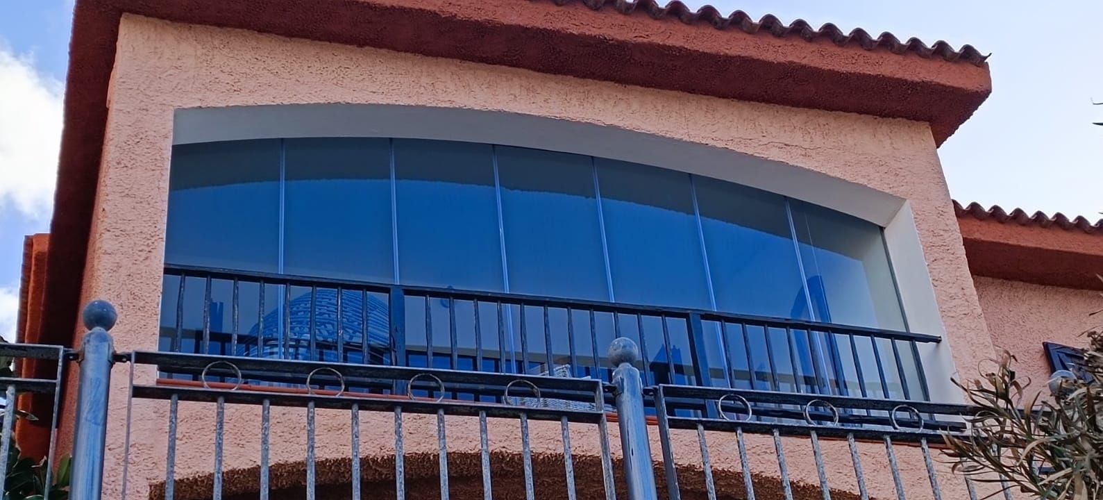 Un edificio con una grande finestra ad arco. La finestra è dipinta di blu e ha una ringhiera nera. L'esterno è color pesca con il tetto rosso.