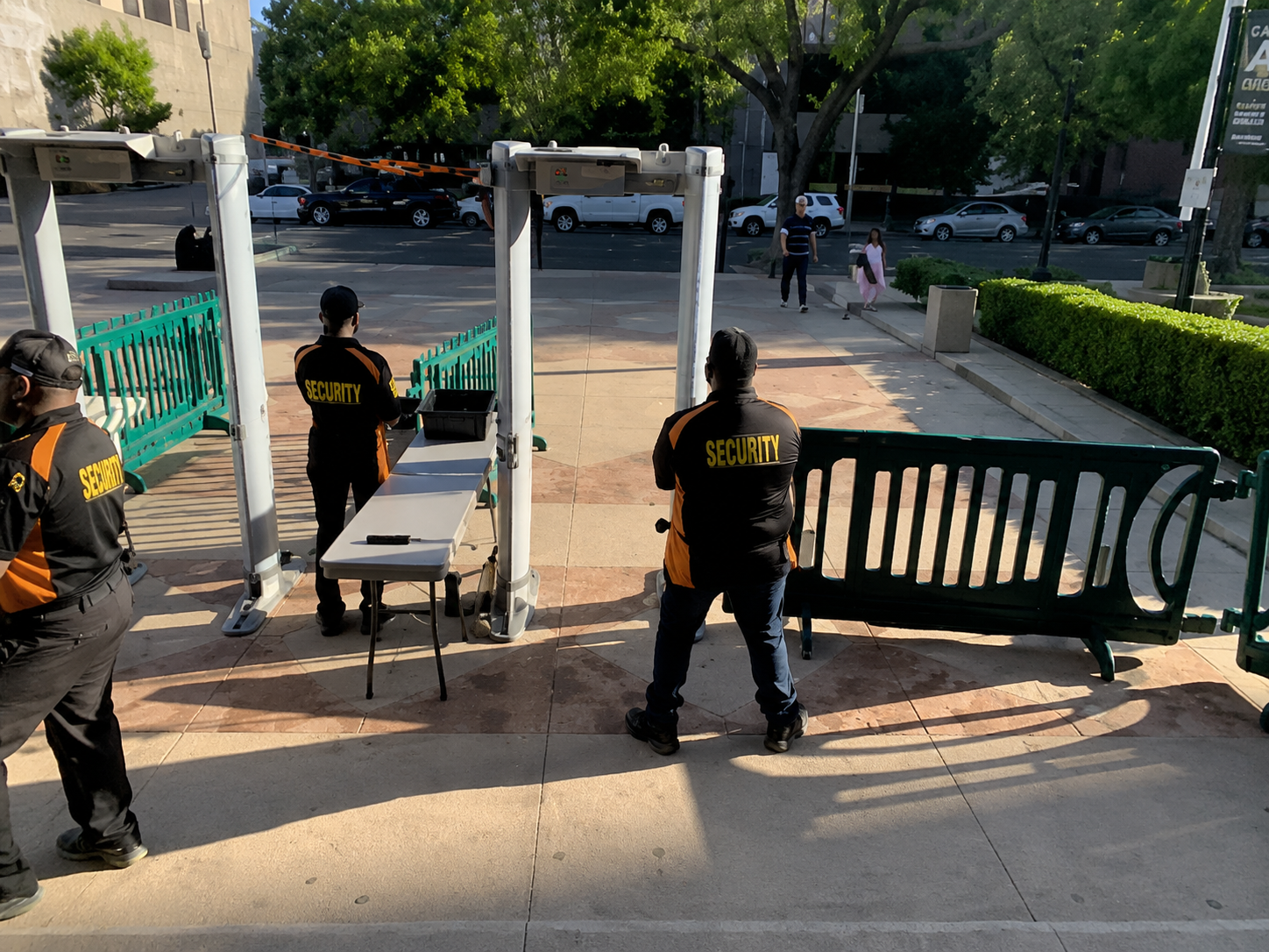 Uniformed security staff move benches and a table at an outdoor courtyard entrance.