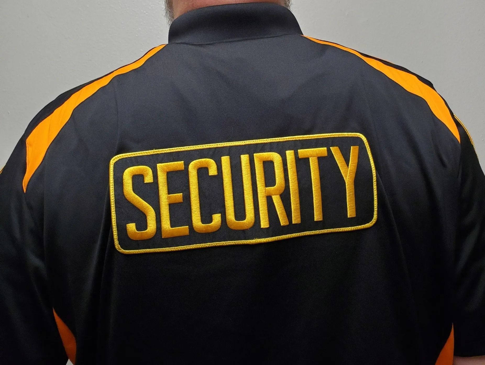 Back of a person wearing a black security jacket with orange stripes and a yellow SECURITY patch