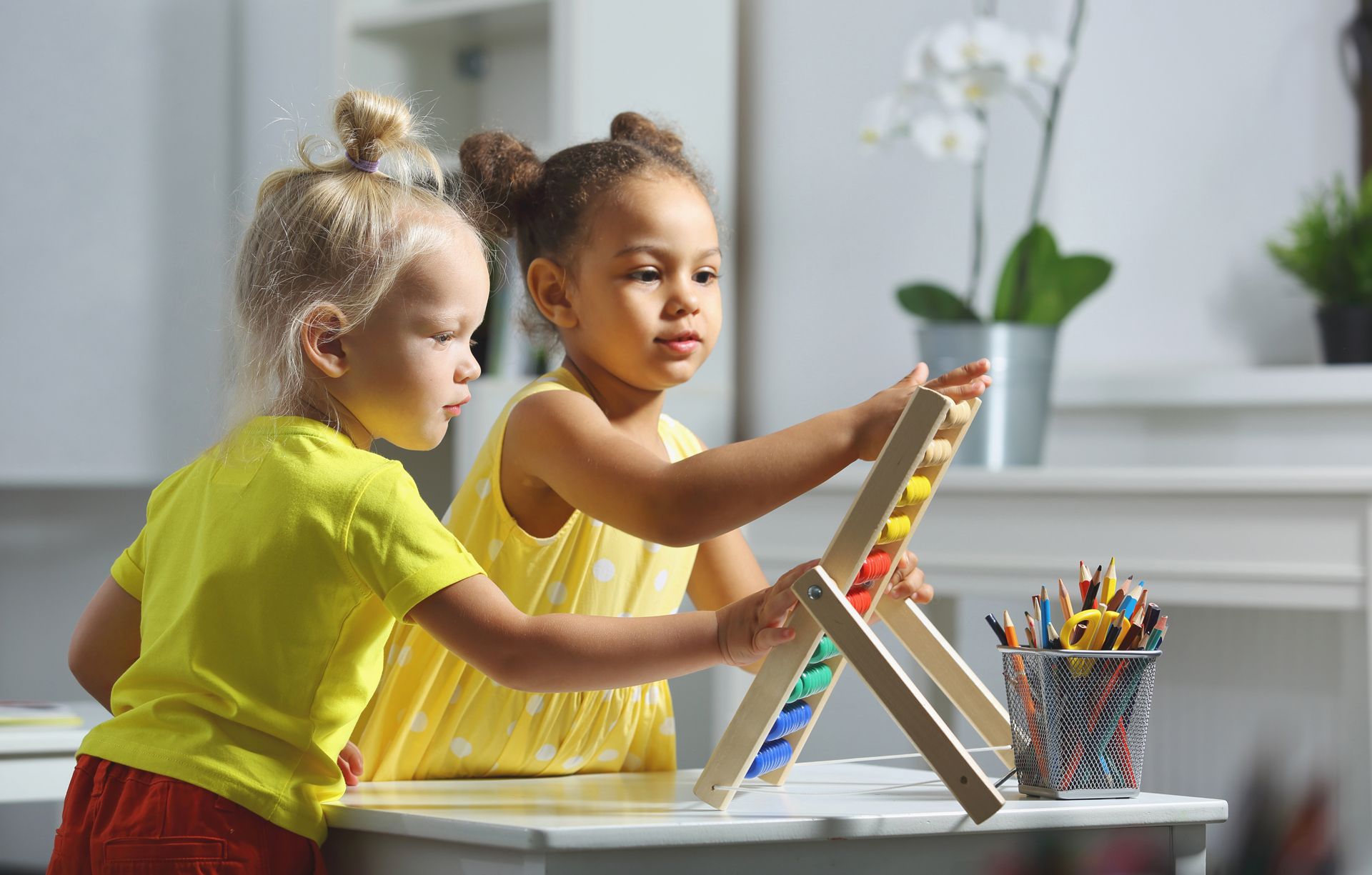 Two little girls are sitting at a table playing with a wooden abacus