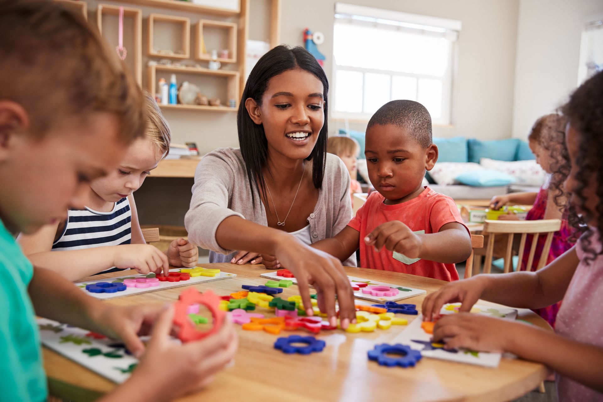 A teacher is playing with a group of children at a table in a classroom