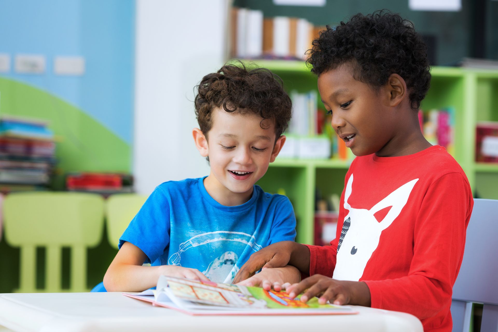 Two young boys are sitting at a table reading a book together