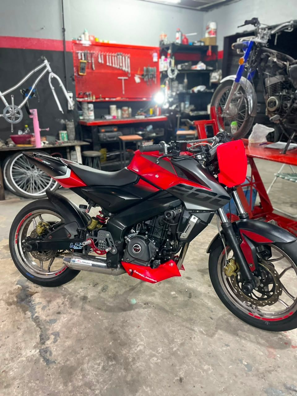 Motocicleta deportiva roja y negra en un garaje con herramientas y otra moto al fondo.