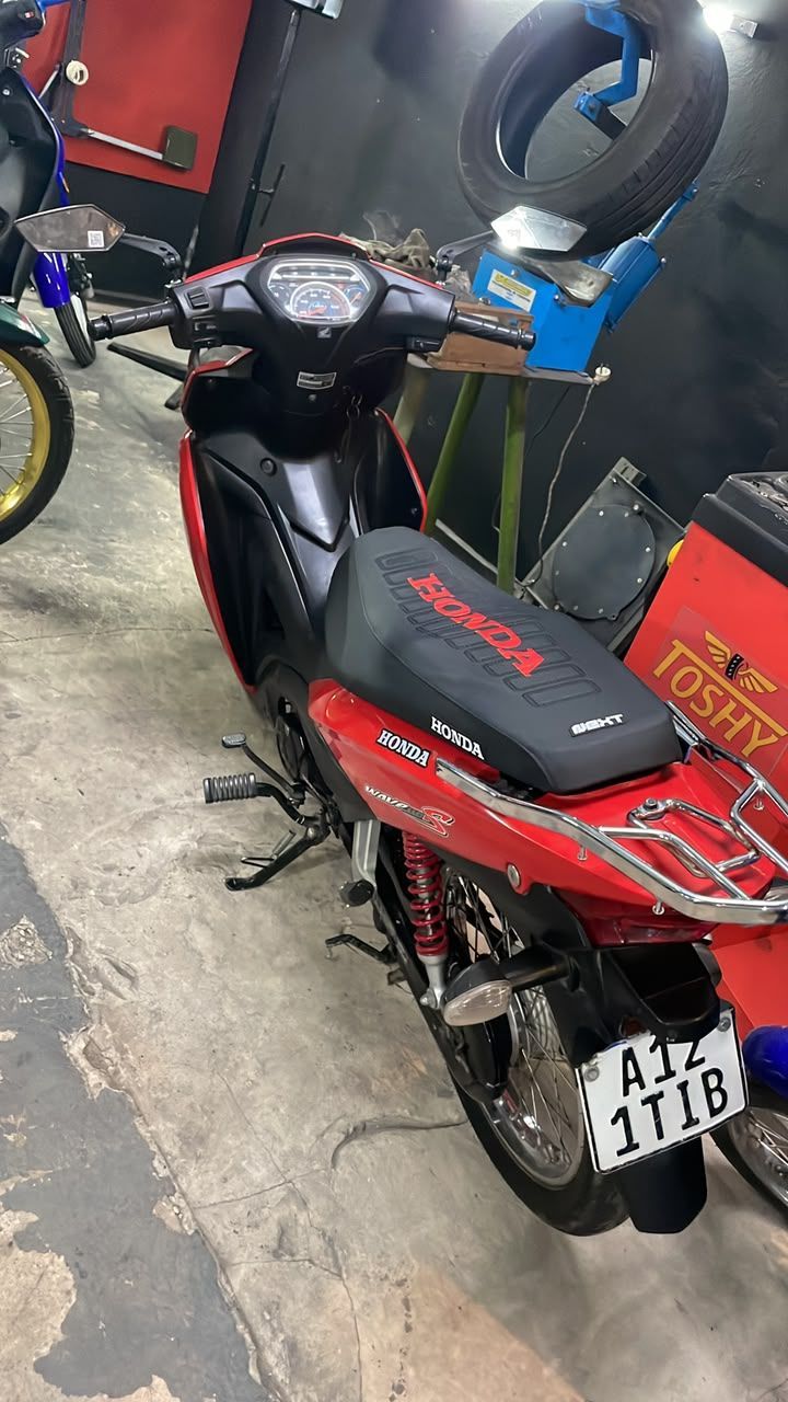 Scooter negro y rojo estacionado en el interior de un taller, visto desde la parte trasera izquierda.