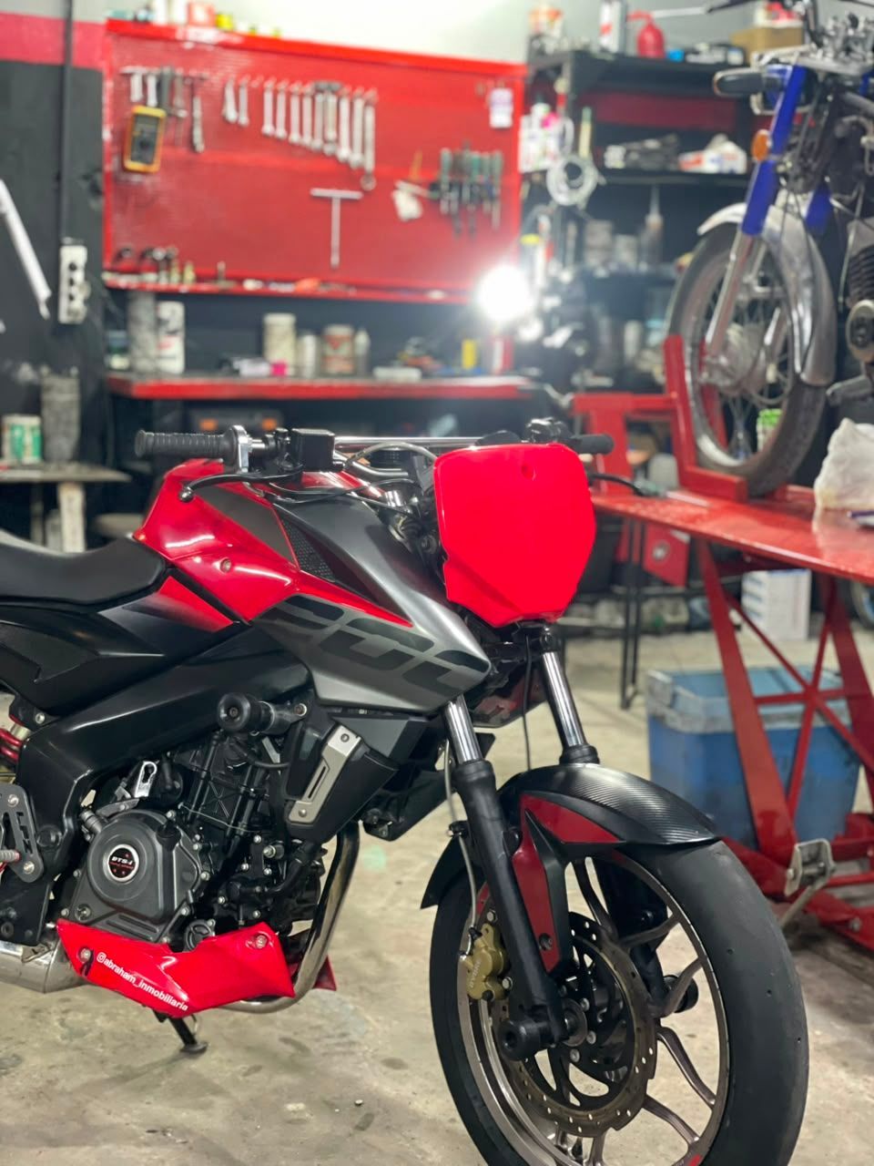 Motocicleta deportiva roja en un taller de motocicletas con herramientas y repuestos al fondo.