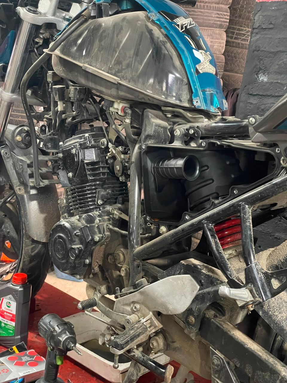 Motocicleta azul gravemente dañada con la parte delantera aplastada en un garaje o taller.